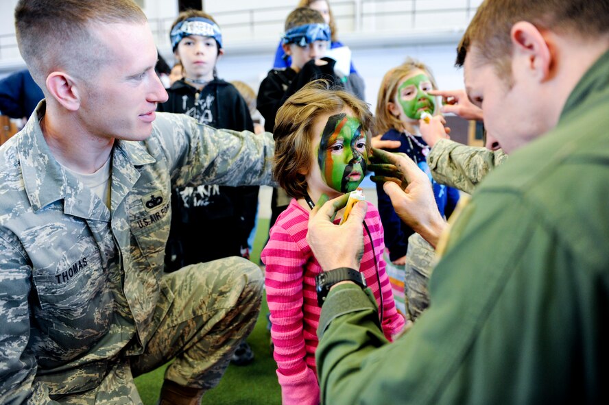 Left) Tech. Sgt. Benjamin Thomas, 28th Security Forces Squadron kennel master, watches as his daughter Gabriel “Gabby” Thomas has her face painted by Senior Airman Brandon Dunphy, 28th Operations Support Squadron survival, evasion, resistance and escape NCO in charge, during “KUDOS, SUDOS and TUDOS,” April 09, 2011, at Ellsworth Air Force Base. The Event held demonstrations from many base organizations in order to inform kids, spouses and teachers about the deployment process. (U.S. Air Force photo/Senior Airman Adam Grant)  