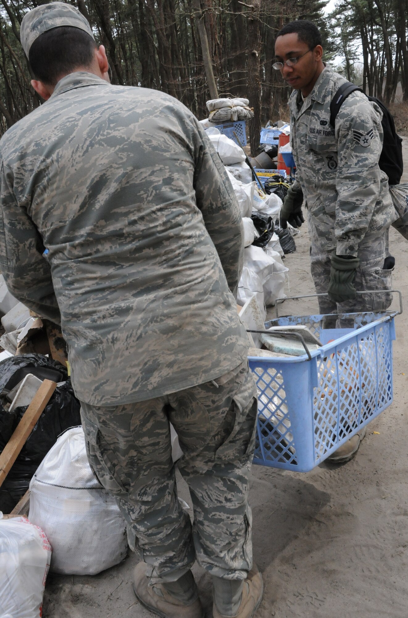 HACHINOHE, Japan – Two 35th Security Forces Squadron Airmen carry a basket filled with styrofoam to a garbage collection point April 7 while cleaning a wooded area in Hachinohe. An 8.9 magnitude earthquake March 11 triggered a devastating tsunami that hit Hachinohe, a northeastern Pacific coastal city about 400 miles north of Tokyo. The tsunami devastated commercial and residential buildings in the area. U.S. military forces make daily trips to Aomori prefecture to help restore the area. (U.S. Air Force photo/Staff Sgt. Erica Picariello)