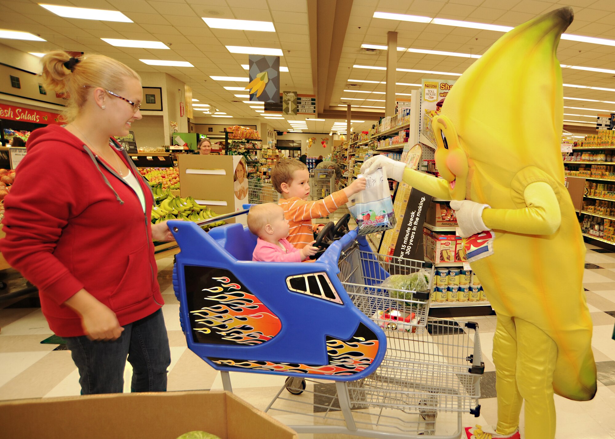 (Far left) Jessi Janes and Ella Grace, Team McConnell family members, watch as “Bobby” the banana gives 4-year-old Lindon Janes a fruit and vegetable goody bag at the base commissary April 7, 2011, McConnell Air Force Base, Kan. The commissary and Maribeth Havran, 22nd Aerospace Medicine Squadron Health and Wellness Center nutrition consultant, provided a healthy foods demonstration to encourage healthy eating and an active lifestyle as part of “Month of the Military Child.” (U.S. Air Force photo/Senior Airman Maria A. Ruiz)
