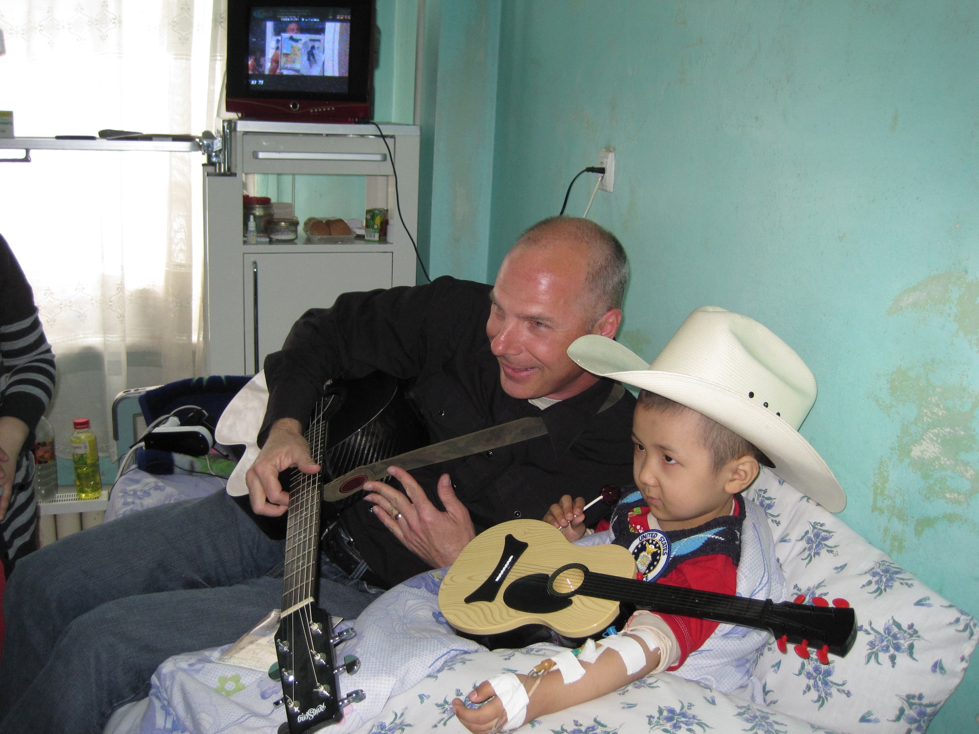 Technical Sgt. Stephen Brannen, AFCENT Band NCOIC, provides a quick guitar lesson to a patient at the Children's Cancer Center in Bishkek, Kyrgyzstan to help keep his mind off from a chemotherapy treatment. (U.S. Air Force photo by Master Sgt. Karl Bradley)