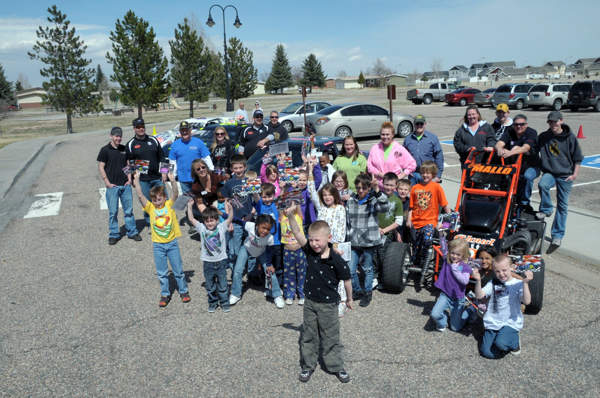 Cheyenne area race car drivers Gary Hobbs, Mark Sopr and his crew chief, Shawn Compton; Cory and Justin Mallo; and BreAnn Adkinson pose for a photo with children at  Warren’s Youth Center, who are displaying autographs they received from the drivers April 8. The visit gave young Warren members a chance to meet some of the local drivers, obtain autographs and get an up-close look at the race cars — even sitting in the driver’s seat. (U.S. Air Force photo by Blaze Lipowski)