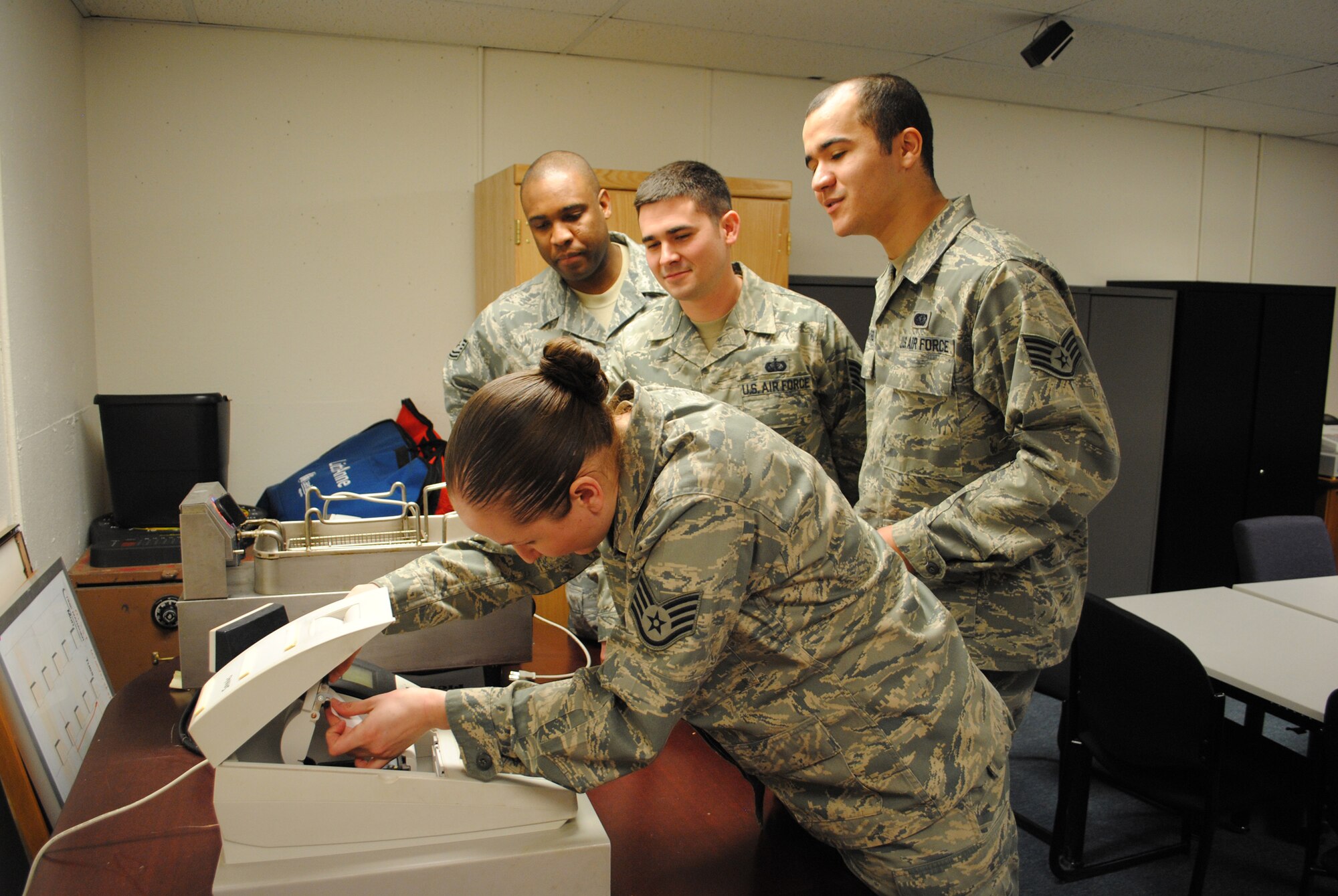 Staff Sgt. Chloe Martin, 10th Missile Squadron assistant noncommissioned officer in charge of missile chefs, demonstrates how to insert reciept paper in a register to (from left to right) Tech. Sgt. Farrel Blake, NCOIC of missile chefs; and Staff Sgts. Erick Dunn, missile chef  trainer, and Ernesto Roman-Cruz, also a missile chef trainers.  How to operate a cash  register is part of the training Sergeant Martin ensures all missile chefs receive before deploying to the field.  (U.S. Air Force photo/Airman Cortney Hansen)