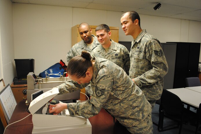 Staff Sgt. Chloe Martin, 10th Missile Squadron assistant noncommissioned officer in charge of missile chefs, demonstrates how to insert reciept paper in a register to (from left to right) Tech. Sgt. Farrel Blake, NCOIC of missile chefs; and Staff Sgts. Erick Dunn, missile chef  trainer, and Ernesto Roman-Cruz, also a missile chef trainers.  How to operate a cash  register is part of the training Sergeant Martin ensures all missile chefs receive before deploying to the field.  (U.S. Air Force photo/Airman Cortney Hansen)