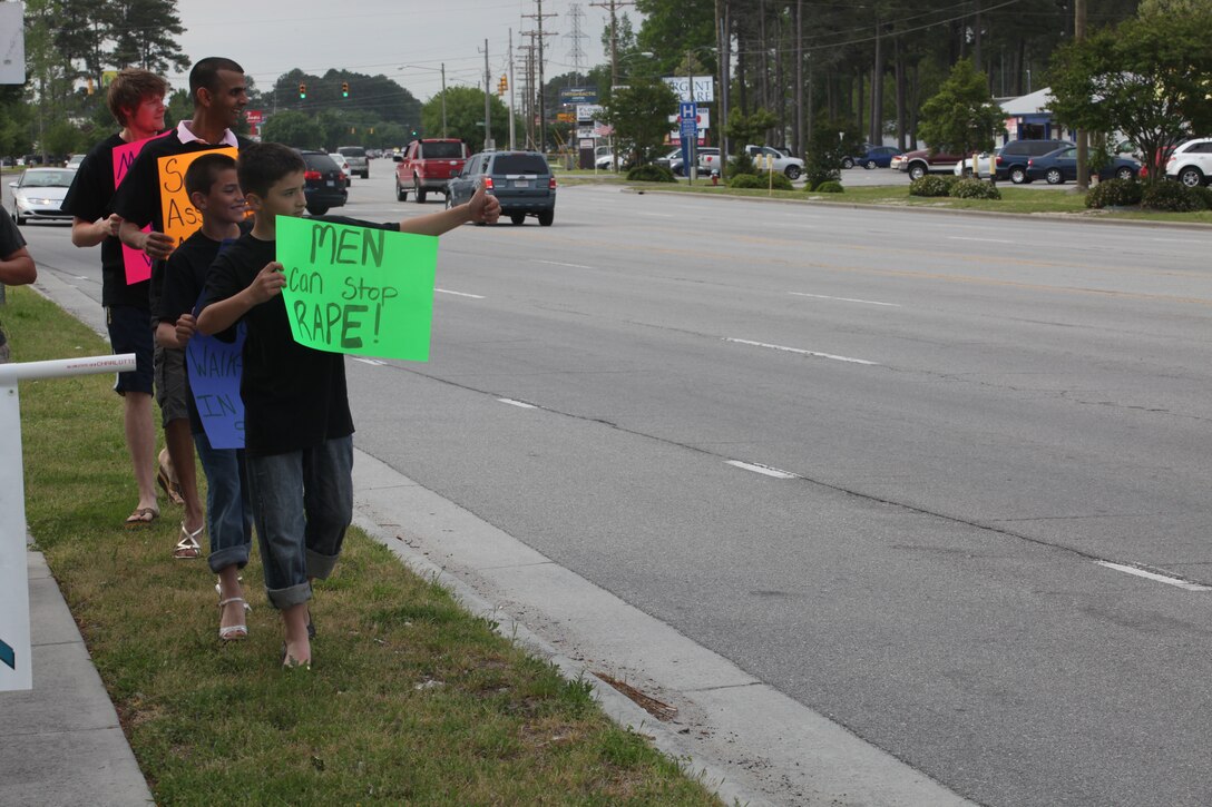 Children, as well as adults, give their appreciation for the show of support from passers-by April 16 on Western Boulevard during the “Walk a Mile in Her Shoes.” More than 150 people joined the march which is an opportunity for men to raise awareness in their community about the serious causes, effects and remediations to sexualized violence.