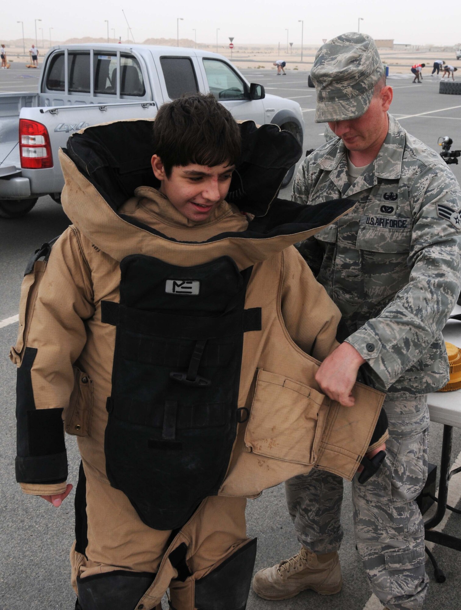 Senior Airman Luke Morse, from the 379th Expeditionary Civil Engineer Squadron explosive ordinance disposal team helps a student from the American School put on an EOD-9 also known as a bomb suit April 14 in Southwest Asia.  Airmen from the 379th Air Expeditionary Wing spent the day with the students participating in different activities. (U.S. Air Force photo/ Staff Sgt. Anthony Graham)