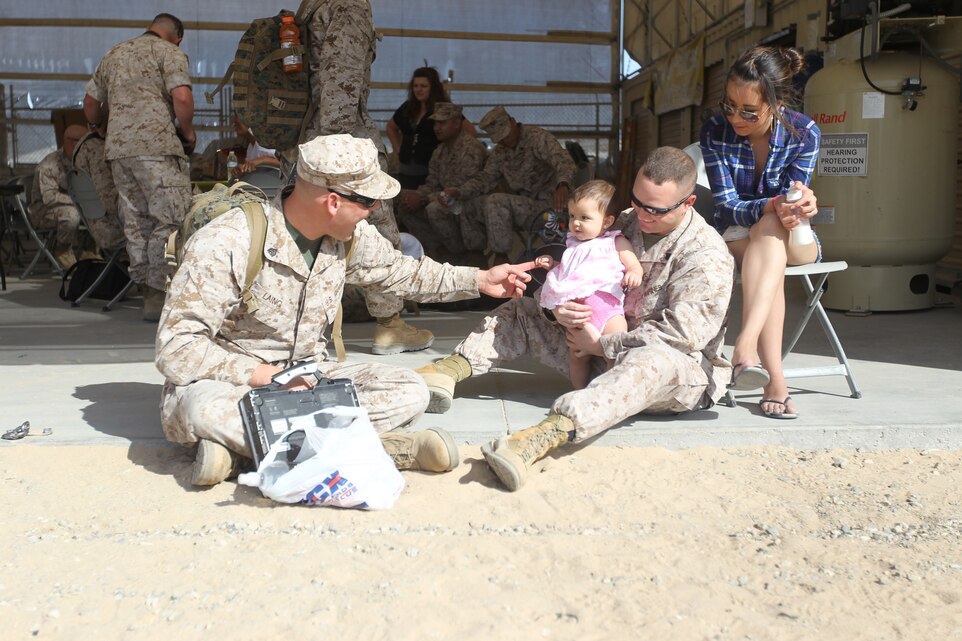 Sergeants Doug Laing [left] and Robert Weinharedt, both unmanned aerial vehicle technicians with the Marine Unmanned Aerial Vehicle Squadron 3, play with Weinharedt’s 8-month-old daughter Isabella, before boarding buses and heading to Helmand Province, Afghanistan, April 19, 2011.::r::::n::