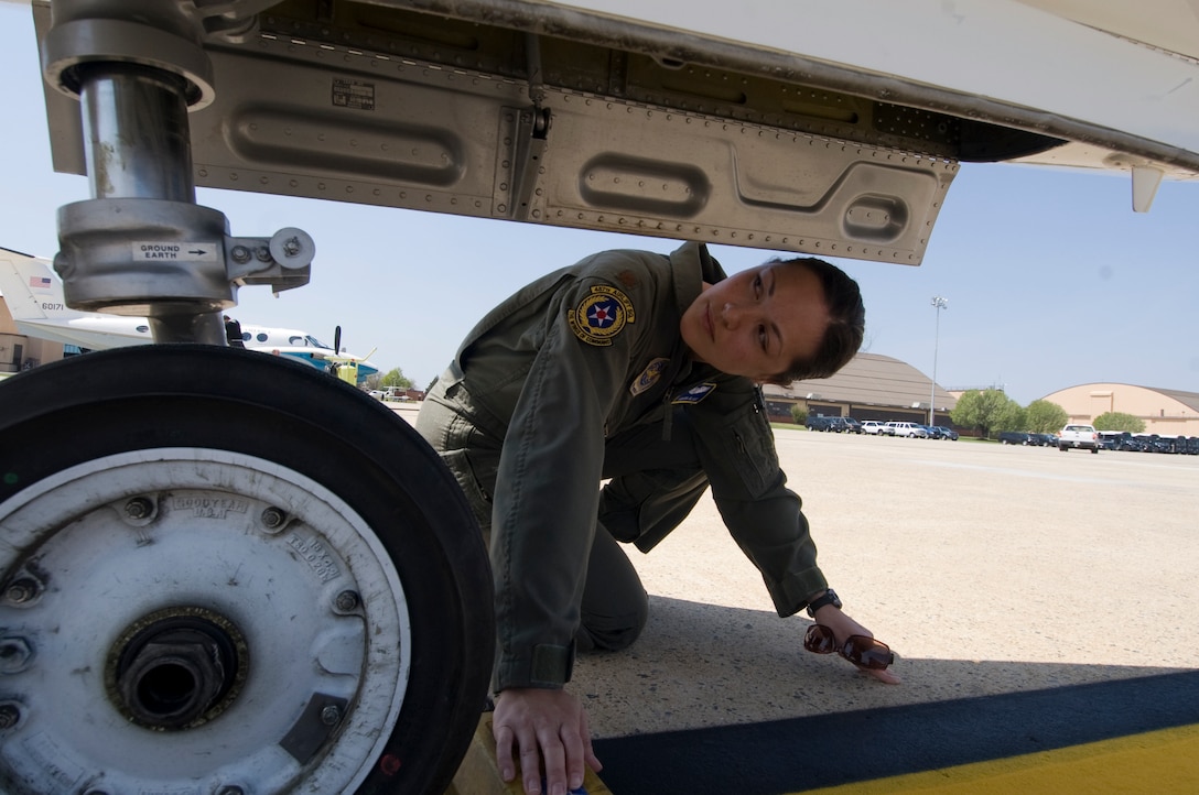 Major Felicia Blair, 457th Airlift Squadron pilot, performs pre-flight checks inside the wheel well of a C-21 squadron aircraft prior to an upcoming mission April 15. (Photo by Bobby Jones)