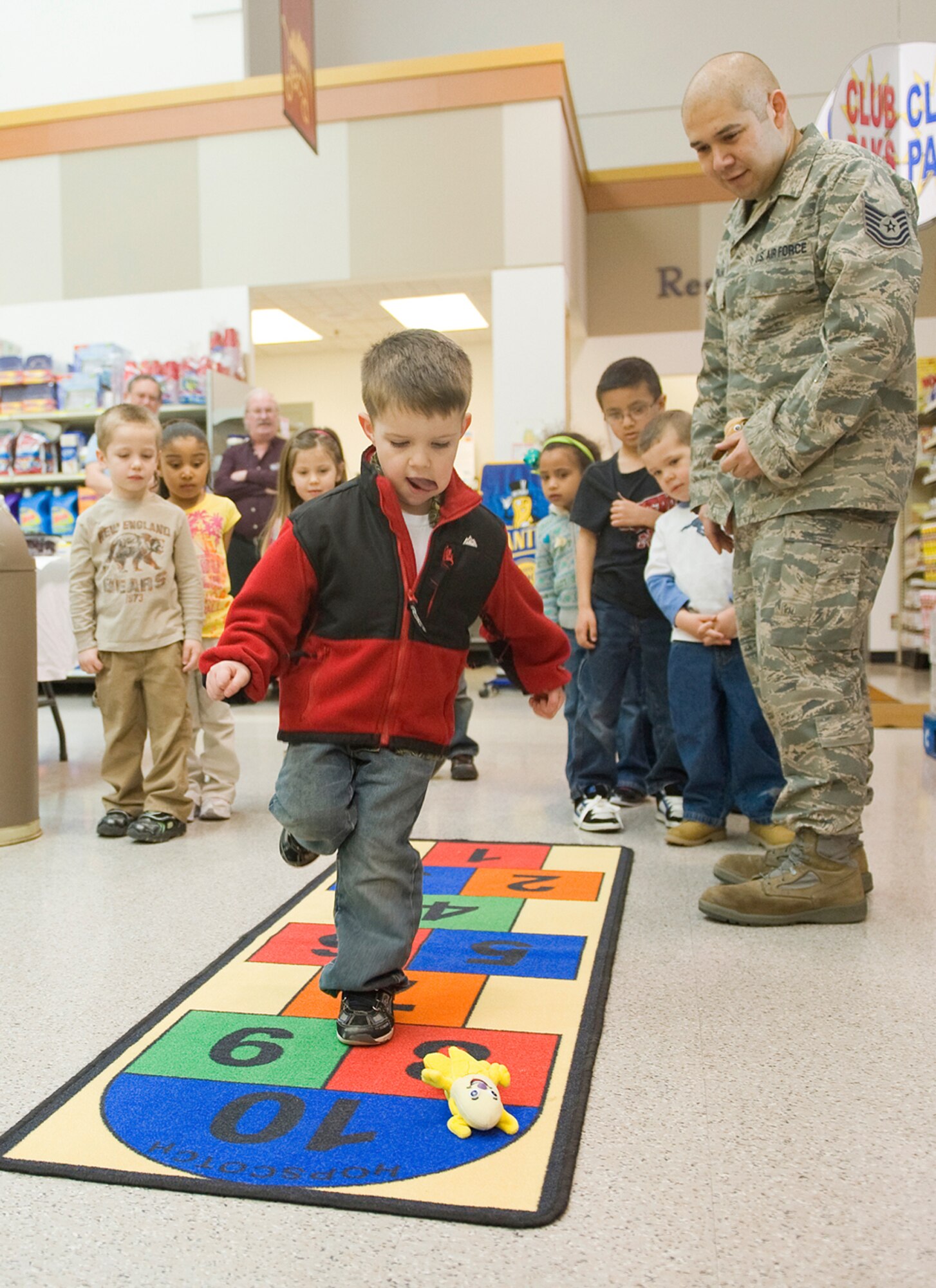 Nathan Griffitts, 4, plays hopscotch at the commissary during the “Month of the Military Child” as Tech. Sgt. Gabriel Carbajal, 341st Medical Support Squadron unit training manager, coaches him April 12. Health and Wellness Center staff were also on hand to lead the children in preparing fruit kabobs to encourage healthy eating habbits. (U.S. Air Force photo/Beau Wade)