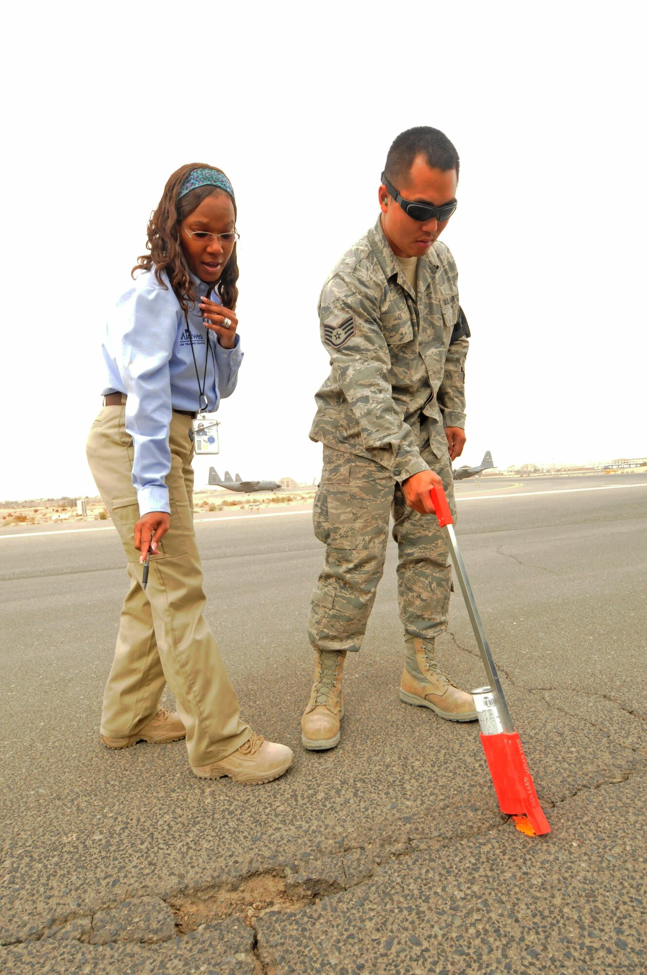 Tiffany Griffin, the assistant airfield manager with the 386th Expeditionary Operations Support Squadron, indicates a hole in the runway for Staff Sgt. Alex Chi, a heavy equipment specialist with the 386th Expeditionary Civil Engineer Squadron, to mark. Sergeant Chi will mark the hole and return another day to fill it. Ms. Griffin is a contractor with Midwest Air Traffic Control Service, Inc., the company who currently overseas the airfield managment and air traffic control services at the 386th Air Expeditionary Wing. Ms. Griffin is originially from Washington D.C. and Sergeant Chi is a New York Guardsman, deployed from the 106th Civil Engineer Squadron. (U.S. Air Force photo by Staff Sgt. Patrice Clarke)