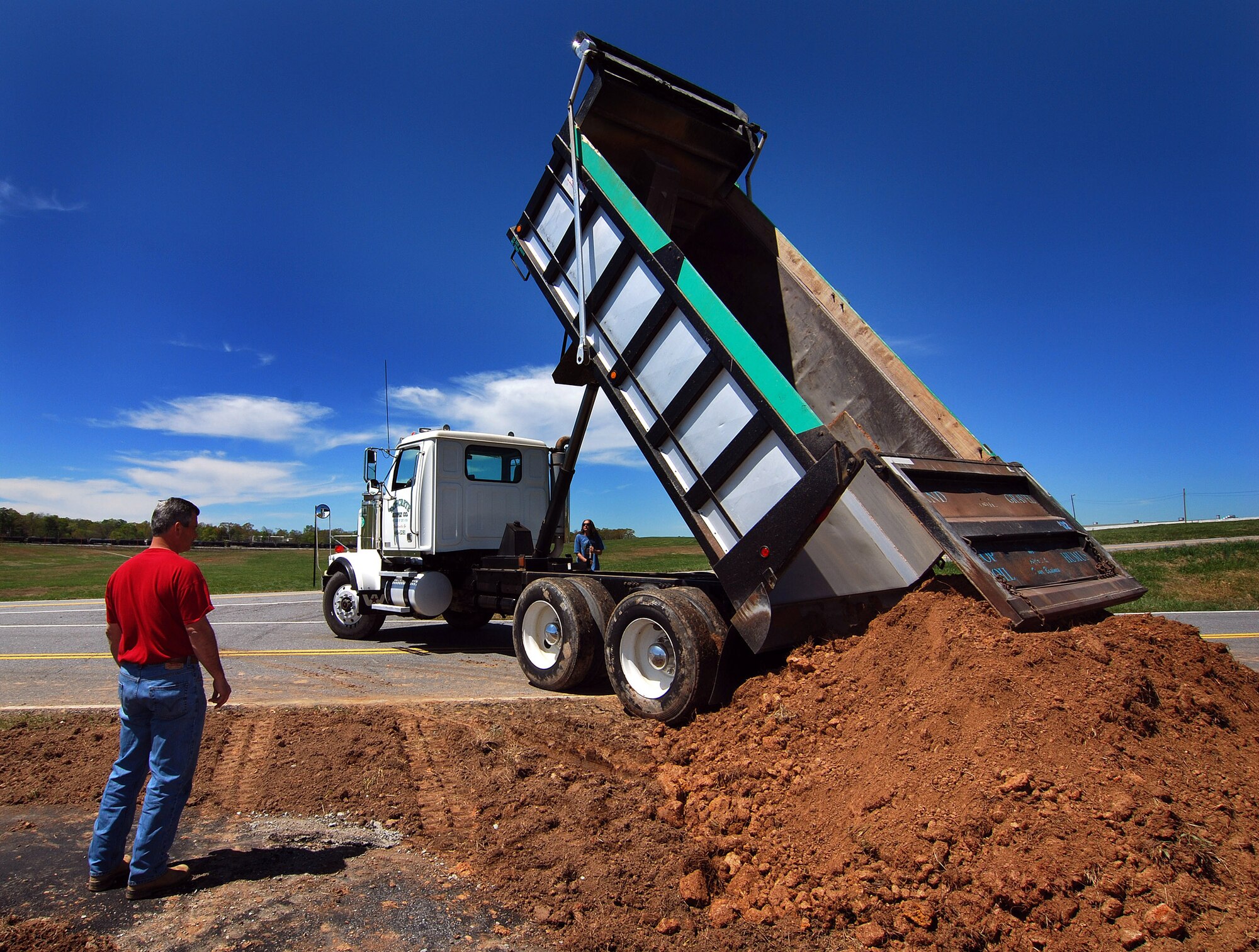 Greg Ivey, of Amber Structures Ltd.,  supervises the offloading of backfill dirt to finish the new west side jogging path on Dobbins Air Reserve Base, Apr 6.  The jogging path is being constructed after several years of planning to connect the Conner's Way trail running from lodging to the B.X. with the Navy path originating from the south side gymnasium so Army Guard soldiers can safely run to that gym.  Soon anyone with base access can run or stroll safely and uninterrupted, from the Dobbins lodging facility all the way to the former Navy gym located on the southwest side of the runway.  (U.S. Air Force photo/ Brad Fallin)