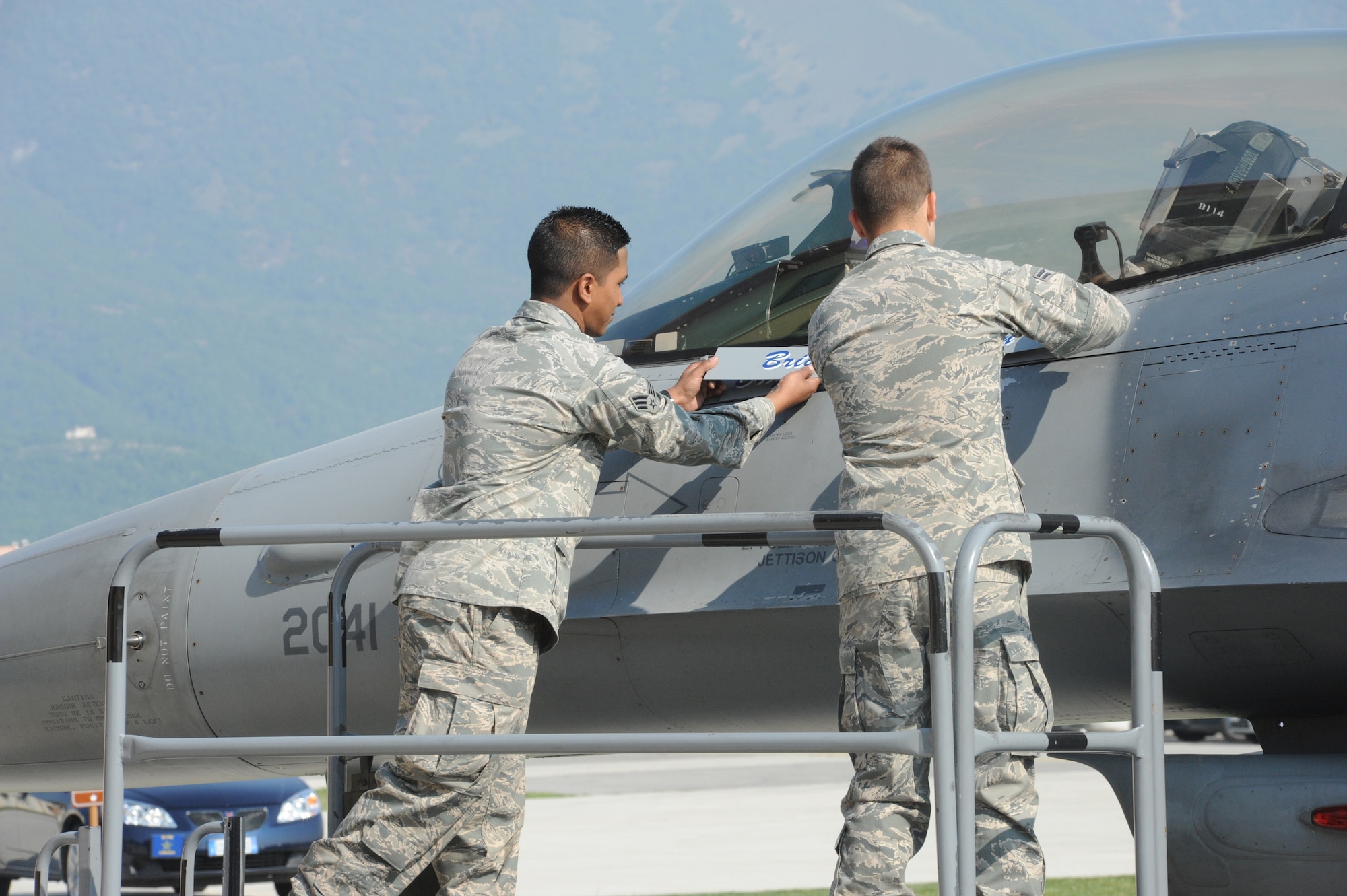 Senior Airman Liam Fernando and Airman 1st Class Mathew Georgion, 31st Aircraft Maintenance Squadron, unveil Brig. Gen. Scott J. Zobrist's name on an F-16 Fighting Falcon during the 31st Fighter Wing change of command ceremony April 22 at Aviano Air Base, Italy. General Zobrist assumed command of the wing, replacing Brig. Gen. Charles Q. Brown Jr., who was selected for reassignment as Deputy Director, Operations (J3), Headquarters U.S. Central Command, MacDill Air Force Base, Fla.(U.S. Air Force photo/Airman 1st Class LaVel Sterling)