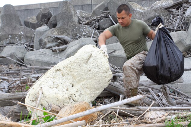 Lance Cpl. David Reyesjimenez, Combat Logistics Company 36 engineer equipment mechanic, gathers trash and debris along the seawall near Penny Lake during an Earth Day celebration here April 22. As residents in the Japanese community, the air station recognizes the month of April as Environmental Awareness Month, a time when station employees and residents are encouraged to continue taking special care of the environment and community they live in.