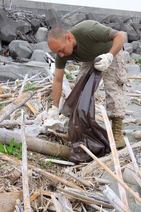 Pfc. David Gonzalez, Combat Logistics Company 36 engineer equipment electrical systems technician, gathers trash and debris along the seawall near Penny Lake during an Earth Day celebration here April 22. When the Marines and sailors were done, the Environmental Department and volunteers hosted a barbeque to thank everyone for the hard work put forth.