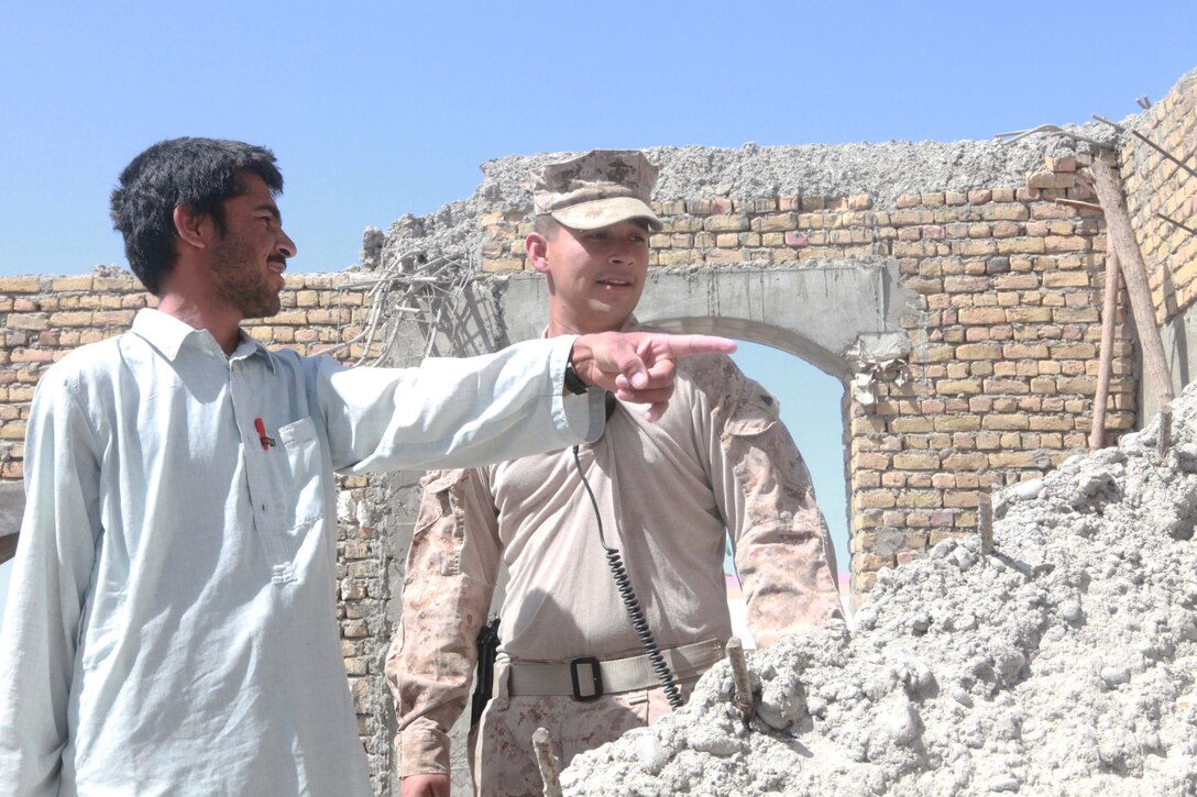 Pomona, Calif., native Cpl. Oscar Llamas observes some debris left over from a building with a collapsed roof in Nawa, Helmand province.  A contractor points to materials he says they can reuse or break down for the reconstruction.  The building, constructed by local contractors, with guidance from both Marines and the local government, will one day host the weekly town meetings held by Nawa citizens.