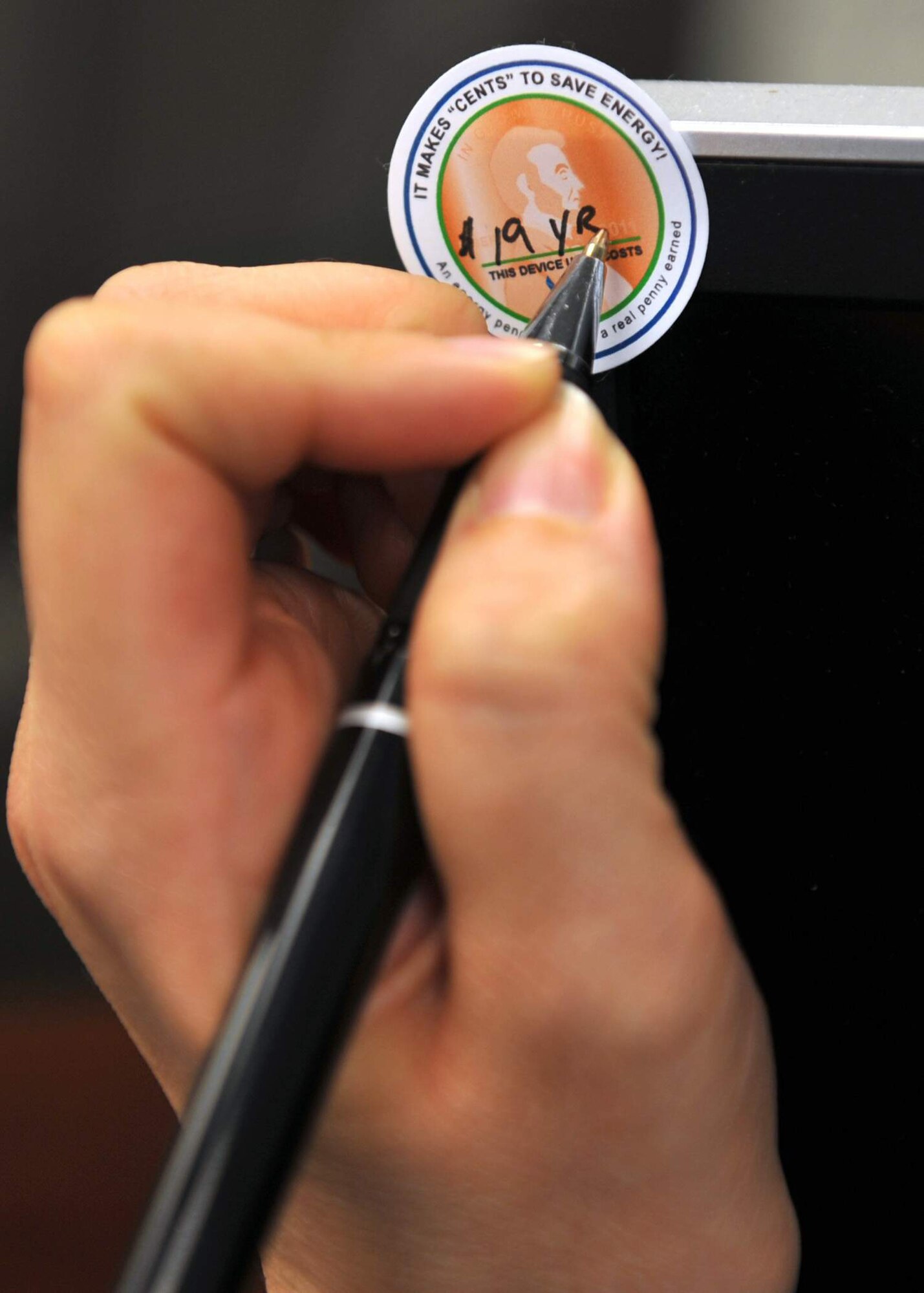 A facility manager at Scott Air Force Base, Ill., marks an energy awareness sticker placed on a computer monitor April 21, 2011. The stickers are meant to bring awareness to the average user about just how much turning on that light switch or computer monitor can cost each day or throughout the course of a year.  (U.S. Air Force photo)