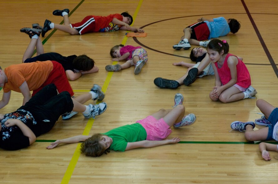 Children in the Luke home pretend to be "beached whales" in a game of "Captain's Coming!" during the physical education program at Luke Air Force Base, Ariz., April 19, 2011. "Captain's Coming" teaches the children to follow directions while using their imaginations to come up with a solution. No two children's "beached whale" is the same. (U.S Air Force Photo/Staff Sgt. Jason Colbert)
