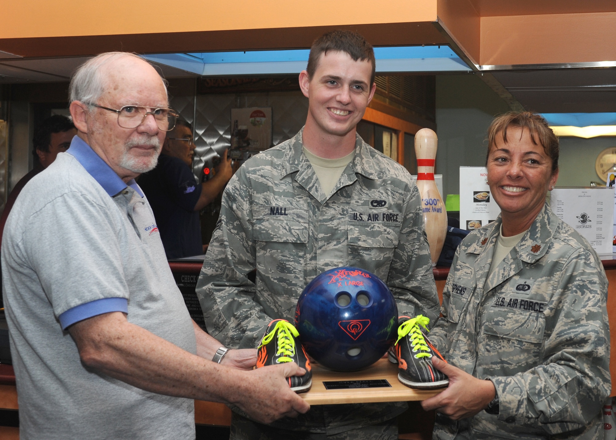 DYESS AIR FORCE BASE, Texas -- Airman 1st Class Kyle Nall, 7th Munitions Squadron, receives a plaque displaying the house ball and shoes used to bowl a 300 April 20 at Dyess Lanes bowling alley here from Wayne Roach (left), Dyess Lanes manager, and Maj. Katrina Stephens (right), 7th Force Support Squadron commander. Airman Nall made Dyess history by becoming the first person to score a 300 bowling while using a house ball and shoes during a sanctioned intramural league on Feb. 23. (U.S. Air Force photo/Airman 1st Class Jenifer H. Calhoun)