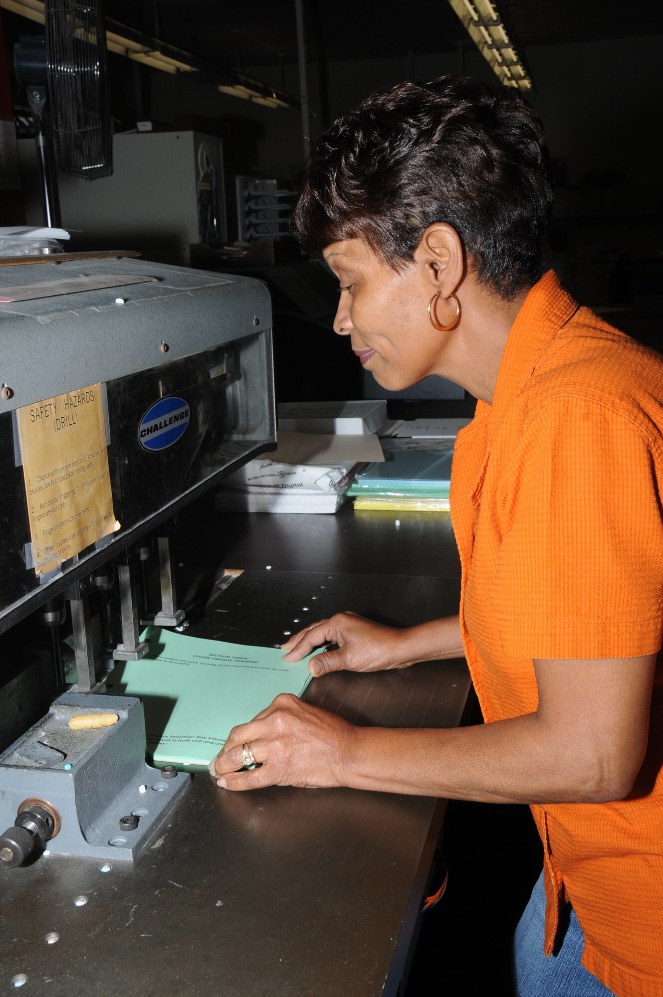Electronic duplication specialist Deborah Johnson uses a hole drillingmachine to prepare a packet of papers.  (U.S. Air Force photo by Kemberly Groue)