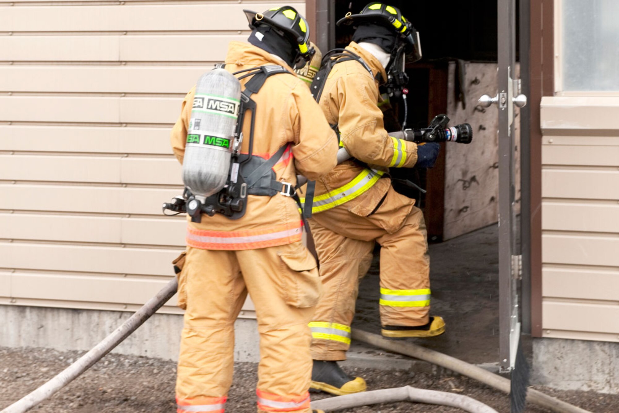 Airman 1st Class Talmage Kinard wields a fire hose during a drill April 22 as Air Force Capt. Jeff Hartley follows him into the mock house to offer instruction and leadership. (U.S. Air Force photo\Johnathon Green)