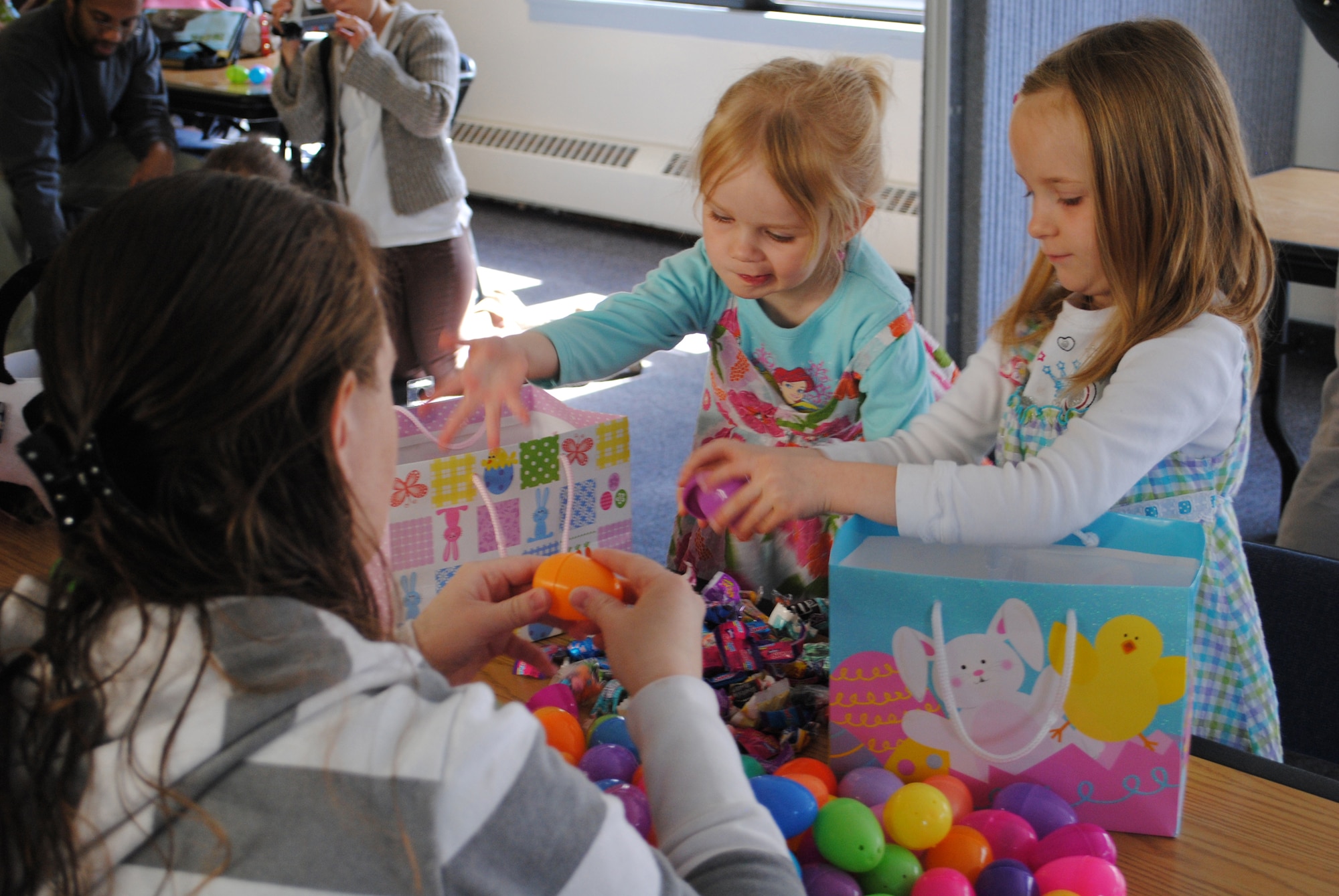 Annabelle, 2 (left) and Abigail, 5, with their mother Angela Wilson, remove the candy and prizes from the eggs they collected from the chapel's Easter egg hunt.  Children walked around the base chapel and collected hundreds of eggs scattered throughout the building.  (U.S. Air Force photo/Airman Cortney Hansen)