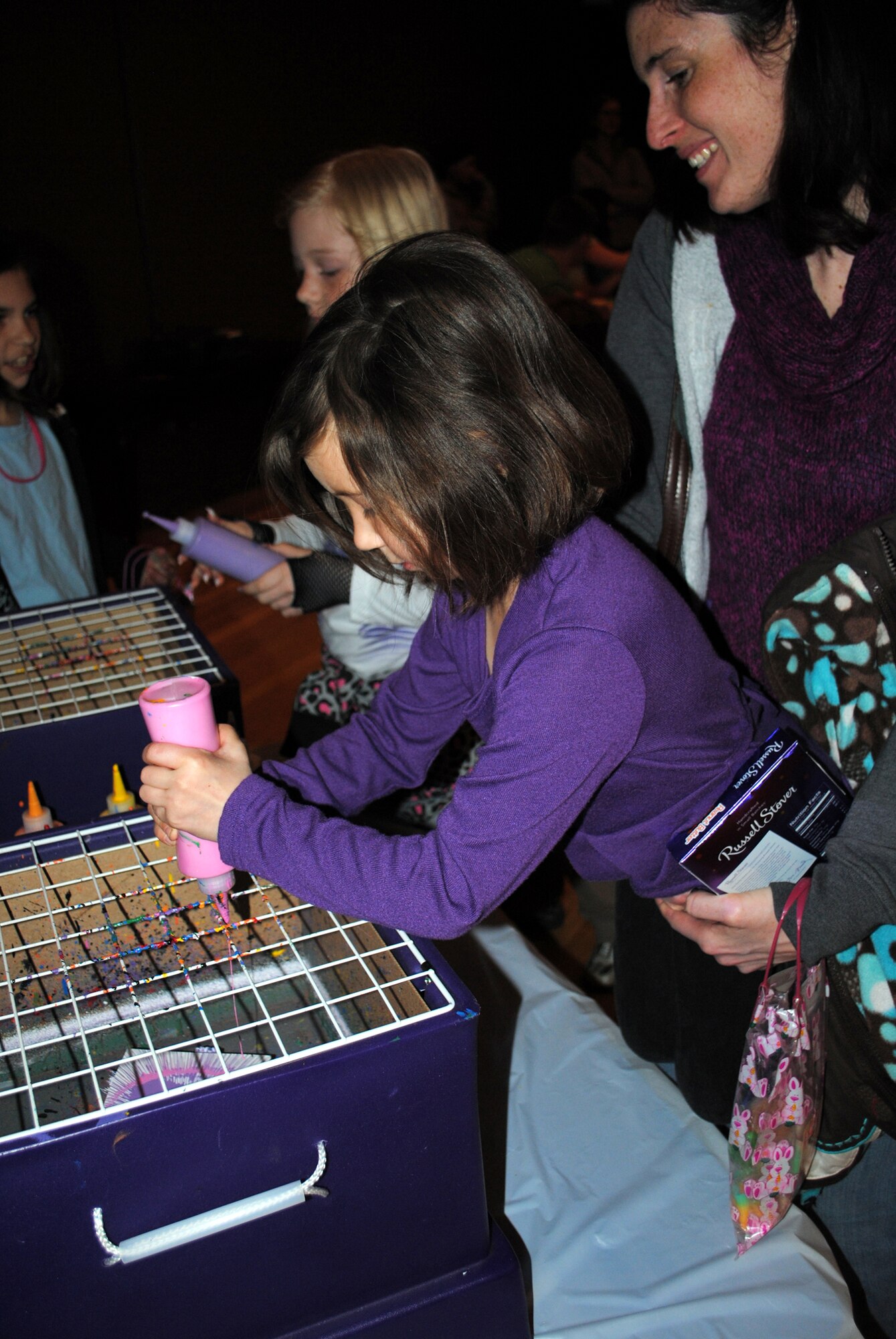 Daisie Clawson, 5, adds pink paint to her soon-to-be finished picture while her mother holds her up to the table.  The paintings were one of many items the children attending the Spring Carnival were able to make and take home with them.  (U.S. Air Force photo/Airman Cortney Hansen)
