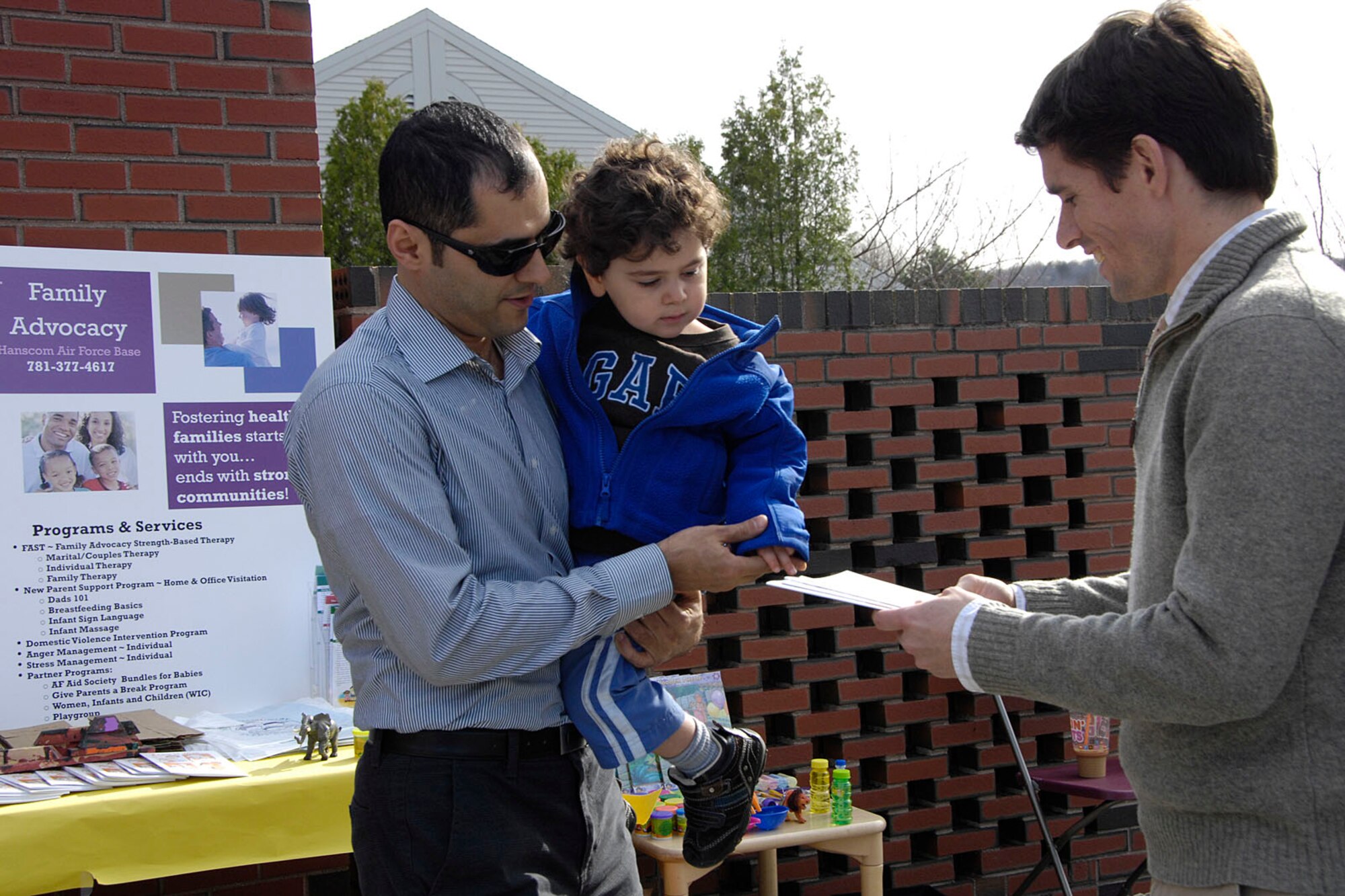 HANSCOM AIR FORCE BASE, Mass. – Matt Nicoli (right), from the Family Advocacy Program, hands information about FAP to Houssam Aboauzahra and his son, Jad, at the Child Development Center April 22. FAP, along with the Base Chapel, CDC Parent Advisory Board, Equal Opportunity Office, Drug, Demand Reduction Program and Airman and Family Readiness Center, provided parents with refreshments in the morning and played games with the kids and parents in the afternoon as part of Family Appreciation Day and Child Abuse Awareness and Prevention Month. (U.S. Air Force photo by Linda LaBonte Britt)