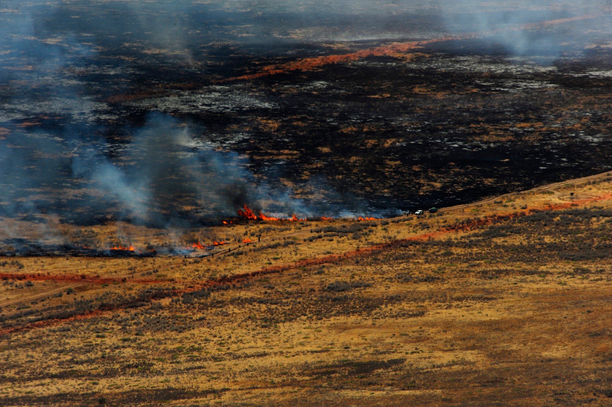 A wildfire burns in West Texas as fire fighting crews try to contain it, April 27, 2011.  Airborne tankers lay lines of red fire retardant to help ground crews contain the fire.  (U.S. Air Force Photo/Staff Sgt. Eric Harris)
