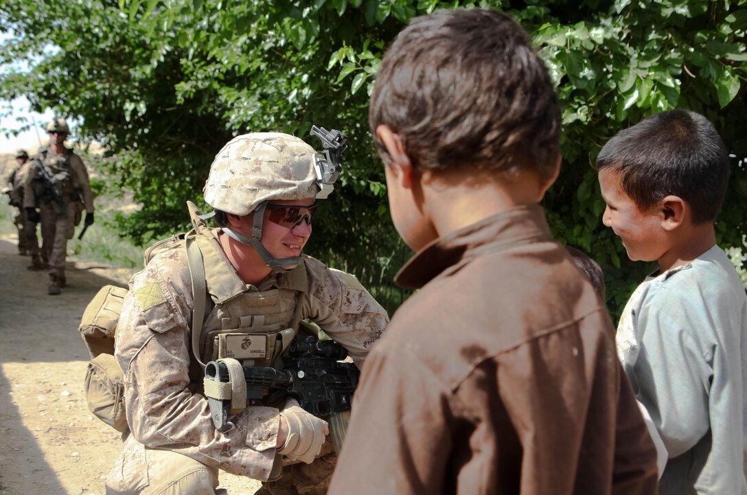 Salem, Ore., Marine Staff Sgt. Benjamin Sundell crouches down to greet local children while on a recent patrol outside the base. Sundell, a platoon sergeant with Company L, 3rd Battalion, 4th Marine Regiment, said he enjoys seeing the children and interacting with them because they are so receptive to the Marines. ::r::::n::::r::::n::::r::::n::