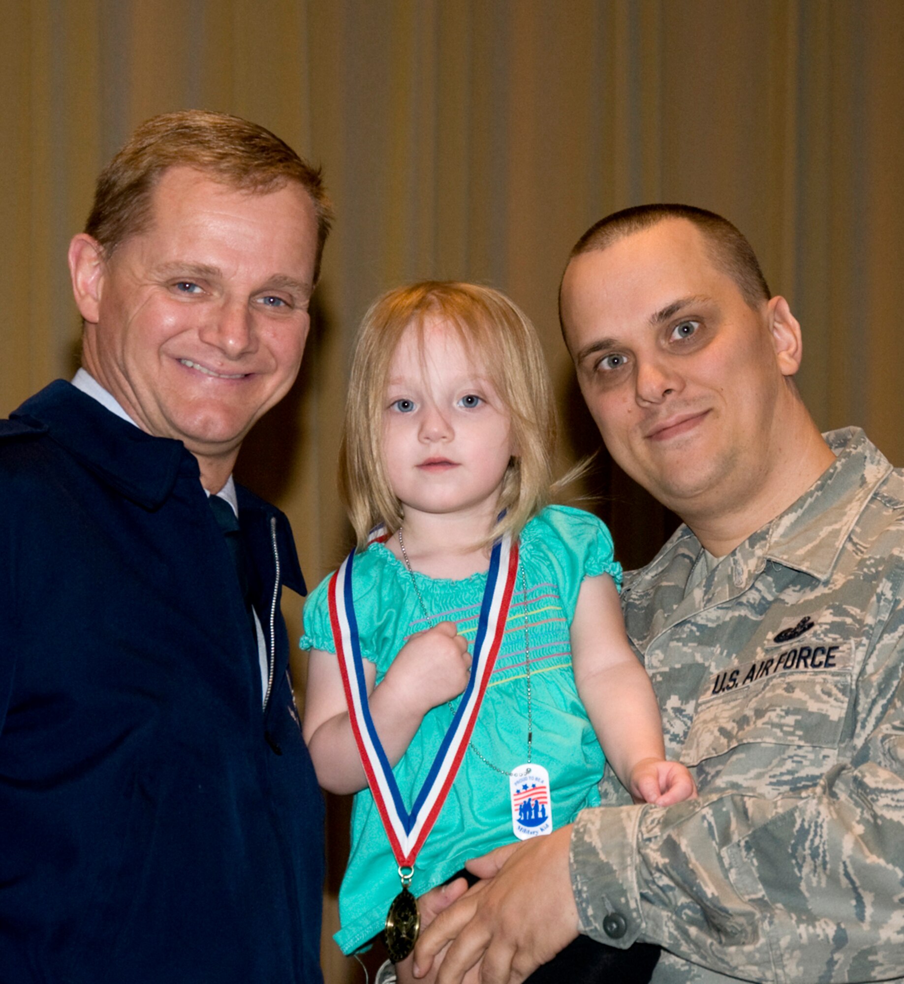 Miriam Harris, center, receives a medal from Col. Russ Mack, the 71st Flying Training Wing commander, left, for being a very helpful military family member. Accompanied by her father, Master Sgt. Troy Harris, right, with the 71st Communications Squadron, Miriam was among 80 children honored at the Military Child Recognition Ceremony held April 28 at Vance AFB. (U.S. Air Force photo/ Roger Betz)