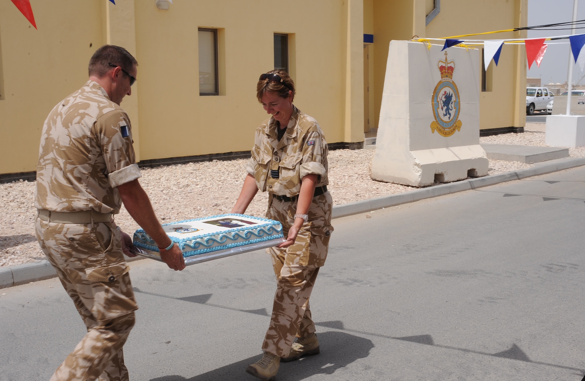 Royal Air Force Sgt. Leigh Williams and Squadron Leader Claire Jennings, carry the cake that U.S. service members made for the celebration of the Royal Wedding during the deployed members' street party, April 29 in Southwest Asia. Street parties are a tradition which has been linked with royal and other national events for a century. (U.S. Air Force photo/Staff Sgt. Liliana Moreno)                                             