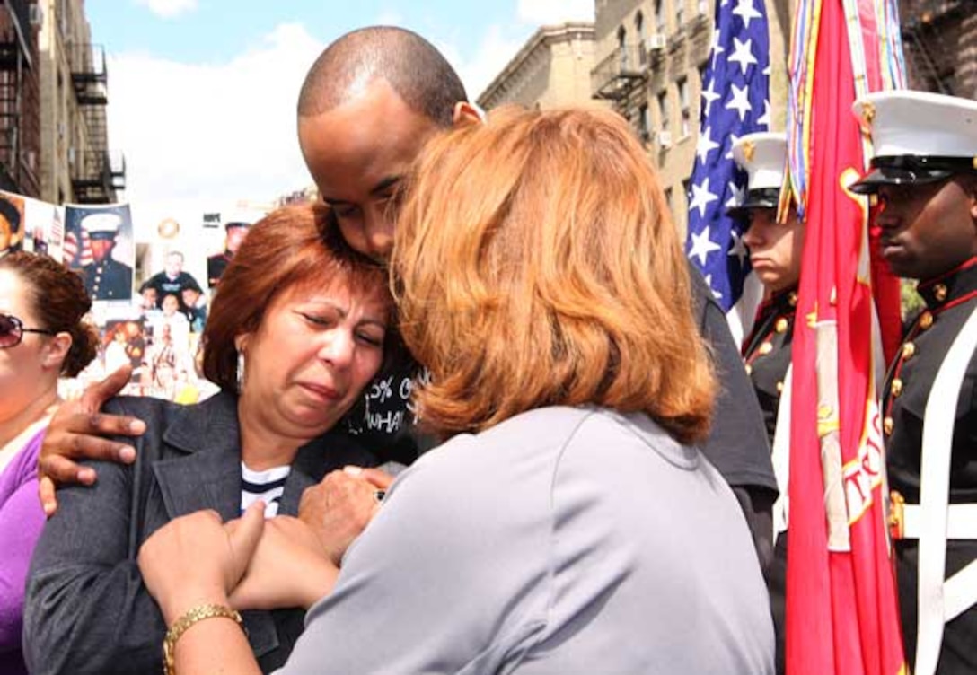 Lourdes German (left), mother of fallen Marine Sgt. Merlin German, receives a hug from Leonardo Blackman, a childhood friend, and Norma Guerra, the executive director of a charity for young burn victims.  The charity, called "Merlin's Miracles", was founded by Sgt. German before he died in 2008.