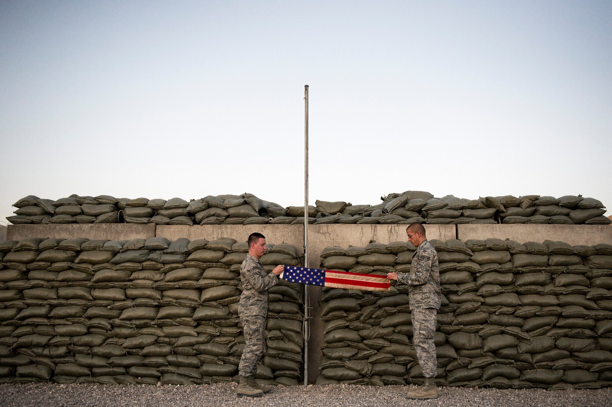 Airman 1st Class Arron Fairfax (left) and Senior Airman Ryan Adkins, Detachment 1, 73rd Expeditionary Air Control Squadron, fold the flag during the daily retreat ceremony at Camp Etchberger. Airmen at the camp perform reveille and retreat ceremonies everyday during their deployment.(U.S. Air Force Photo/Master Sgt. Jeffrey Allen)