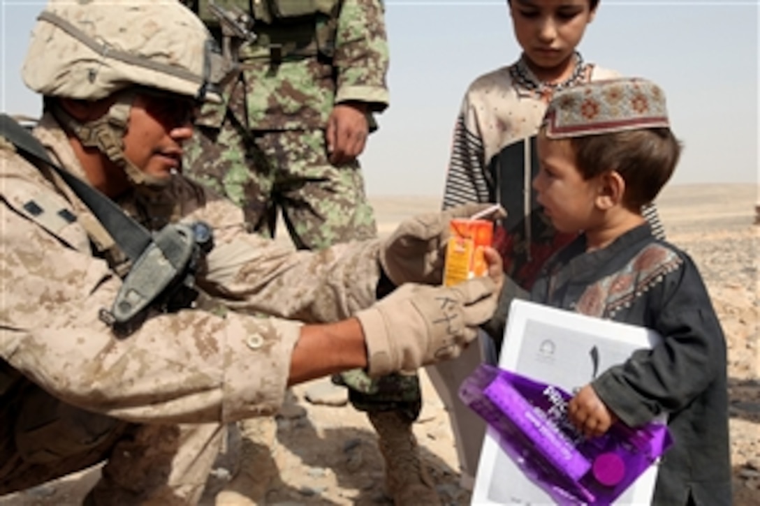 Cpl. Henry Garza, a turret gunner with Company C, 1st Battalion, 23rd Marine Regiment helps an Afghan child learn to drink from a juice box during a patrol near Camp Leatherneck, Helmand province, Afghanistan, on July 28, 2011.  