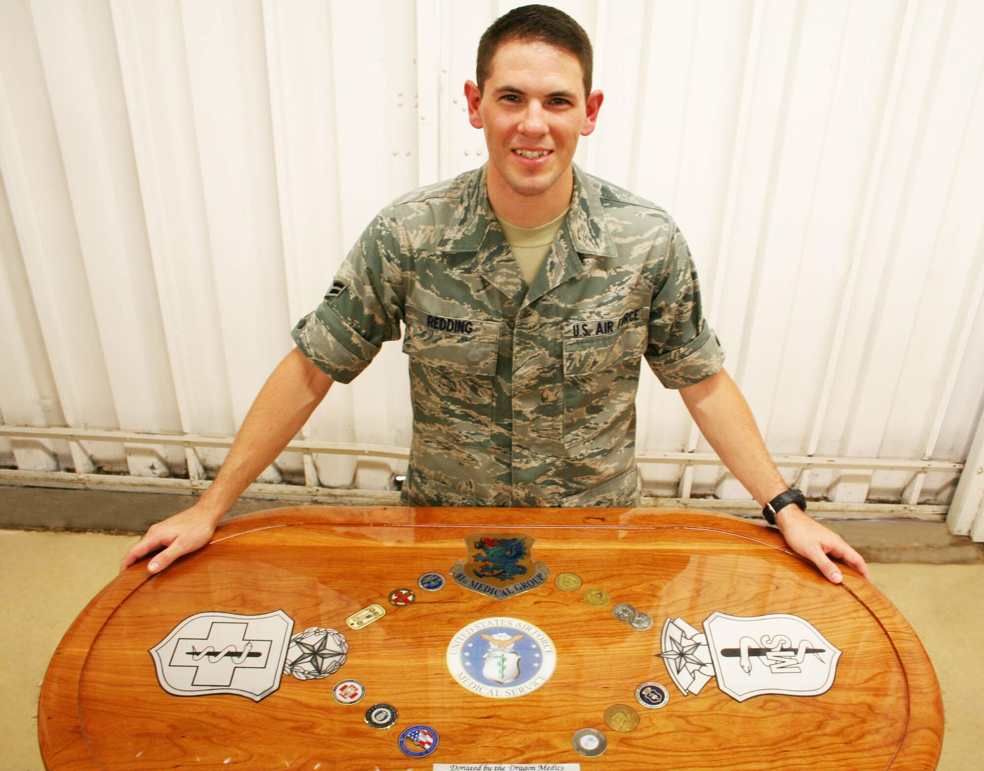 Airman 1st Class David Redding, pictured, 81st Medical Support Squadron, and Staff Sgt. Jim Hampton, another squadron member, presented the Bay Breeze Event Center with a hand-crafted table for the collocated lounge. The cherry wood and polyurethane table is inlaid with coins from each of the 81st Medical Group  squadrons. Redding and Hampton began the project in May at the arts and crafts center wood-working shop.  (U.S. Air Force photo by Eva Ferrell)