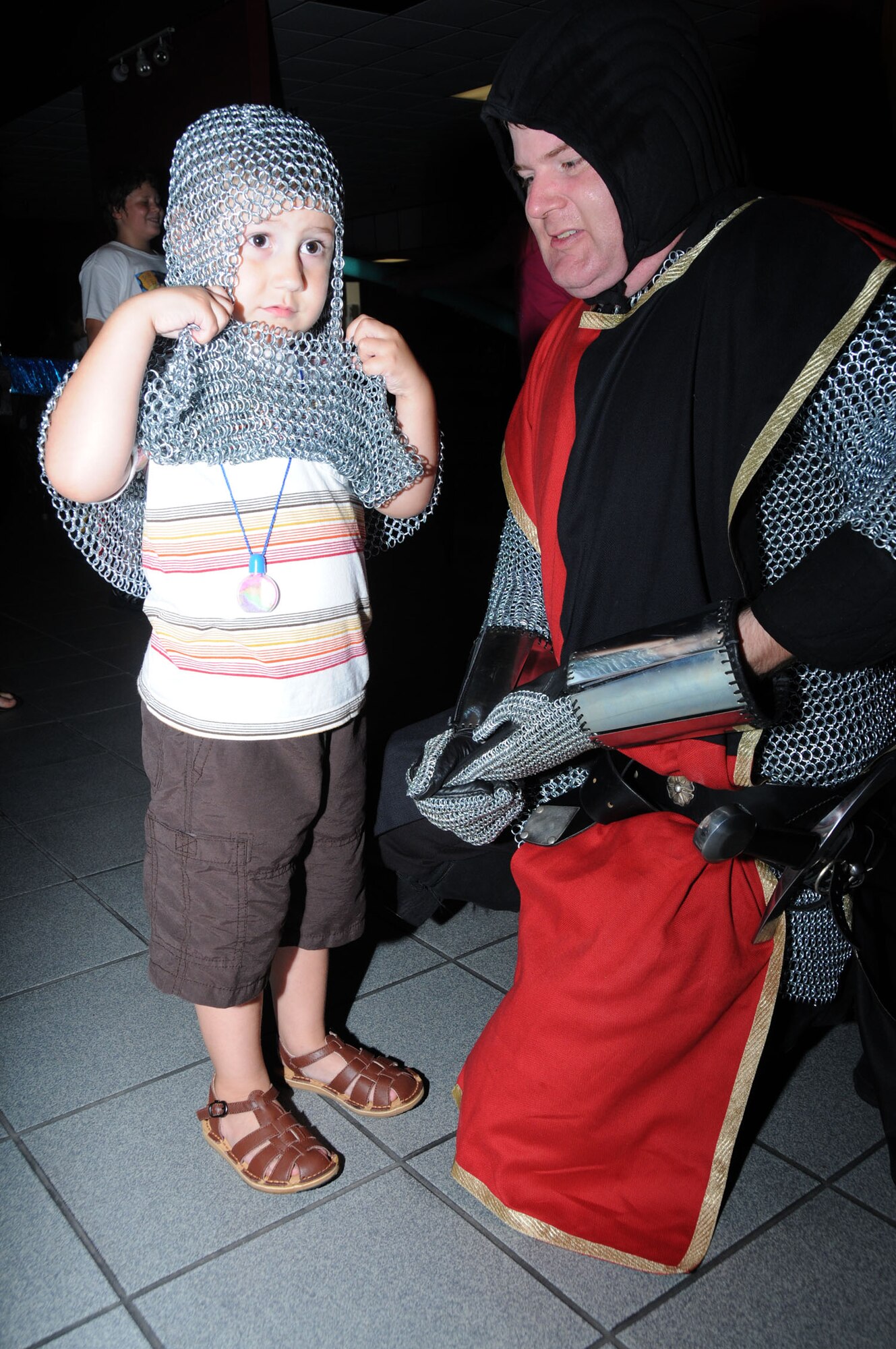 Alexander Doré, 3, prepares for battle by trying on a chain mail coif from Tech Sgt. Christopher Litton, 81st Communications Squadron.  Litton is wearing a dismounted knight’s uniform during the Medieval Faire, the finale to the A Midsummer Knight’s Read summer reading program at McBride Library. The Medieval Faire was held at the Vandenburg Community Center July 28.  Alexander is the son of Capt. Dean and Tara Doré, 81st Inpatient Operations Squadron.  (U.S. Air Force photo by Kemberly Groue)