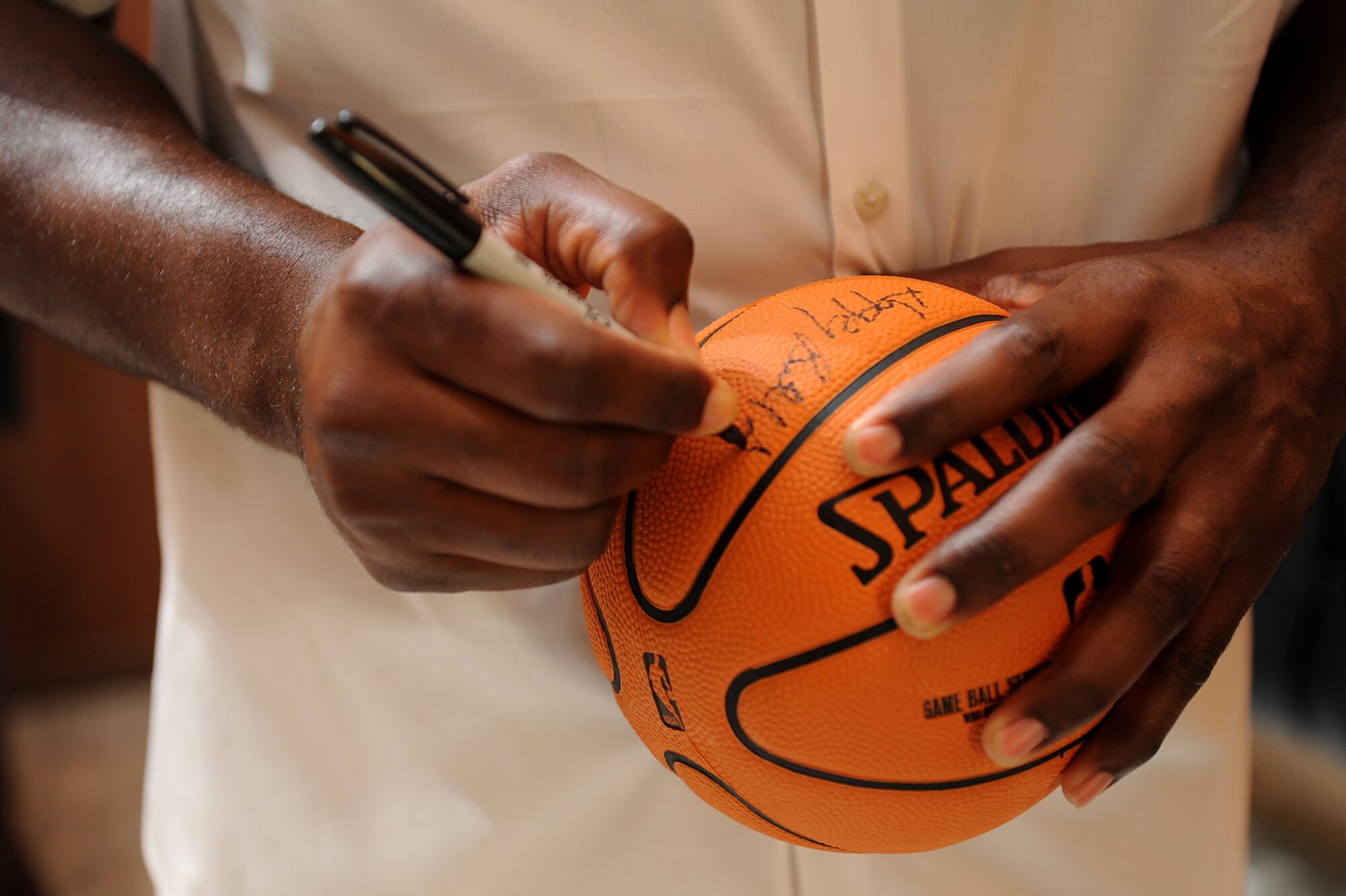 Karl Malone autographs a souvenir during a United Service Organization, or USO appearance at Sather Air Base, Iraq, Aug. 2, 2011. Malone, former National Basketball Association professional basketball player, and David Blaine visited Airmen here as part of a three country, six-day USO tour. (U.S. Air Force photo/Staff Sgt. Mike Meares)