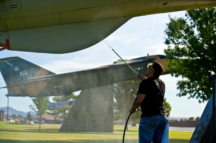 U.S. Air Force Senior Airman Matthew Byous, 57th Aircraft Maintenance Squadron crew chief, power washes the bottom of a F-105 Thunderchief static display July 29, 2011, at Nellis Air Force Base, Nev. Senior Airman Byous is among a group of volunteers from the 57th and 757th Aircraft Maintenance Squadrons that washed the airplane static displays for the first time in a new plan to wash them once every quarter. (U.S. Air Force photo by Airman 1st Class George Goslin/Released)