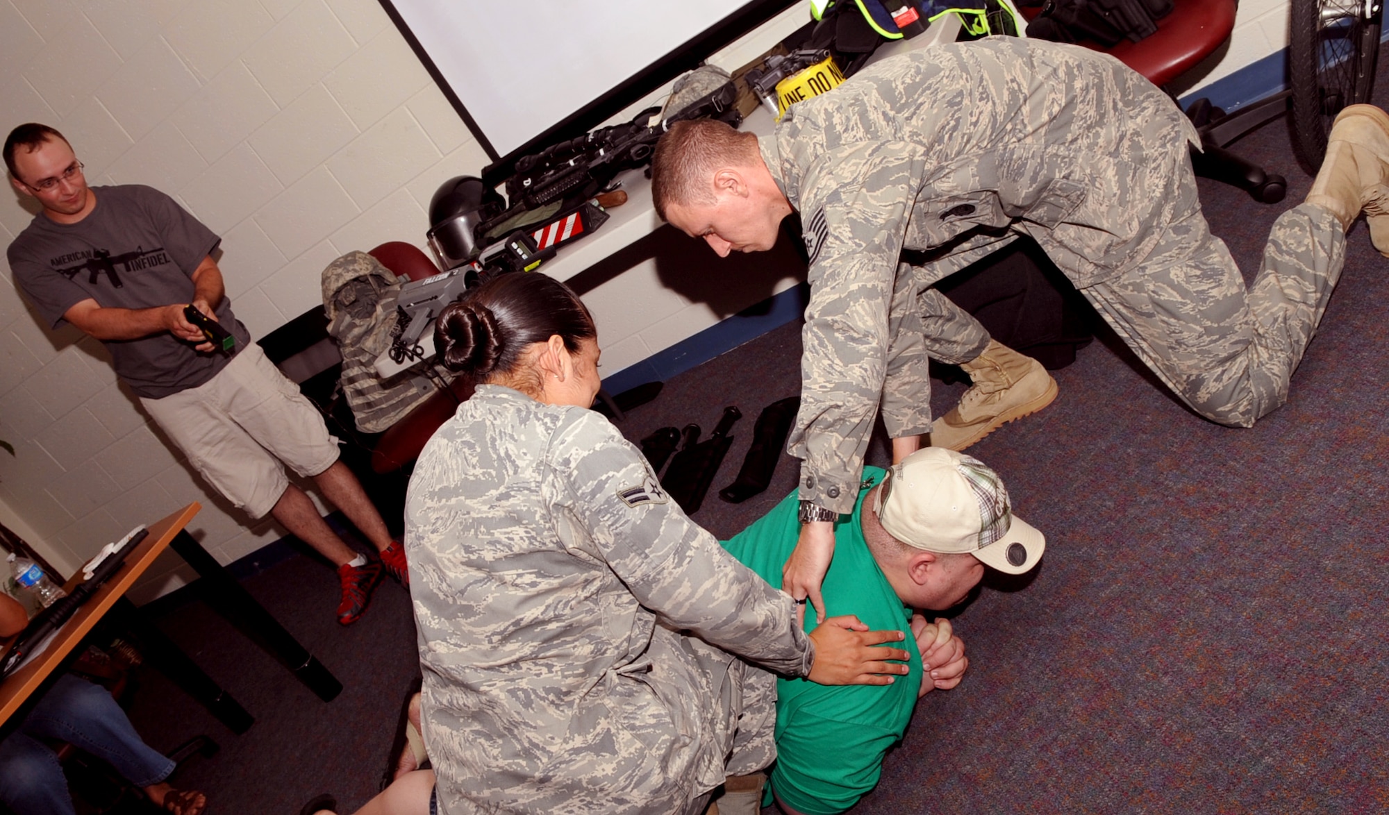 Tech Sgt. Christopher Beavers, 633rd Security Forces Squadron NCOIC of community policing, and Airman 1st Class Stephanie Miller, 633rd SFS Community Police patrolman hold Citizens' Police Academy participant Ned Pitlock for safety as A1C Adrien Dupuis, 633rd SFS Community Police patrolman, demonstrates how a taser feels during a class at Bethel Manor Aug. 4, 2011. The academy is an eight week course in which participants can witness demonstrations of tools and equipment used by security forces members.  (U.S. Air Force photo by Staff Sgt. Logan Tuttle/Released)