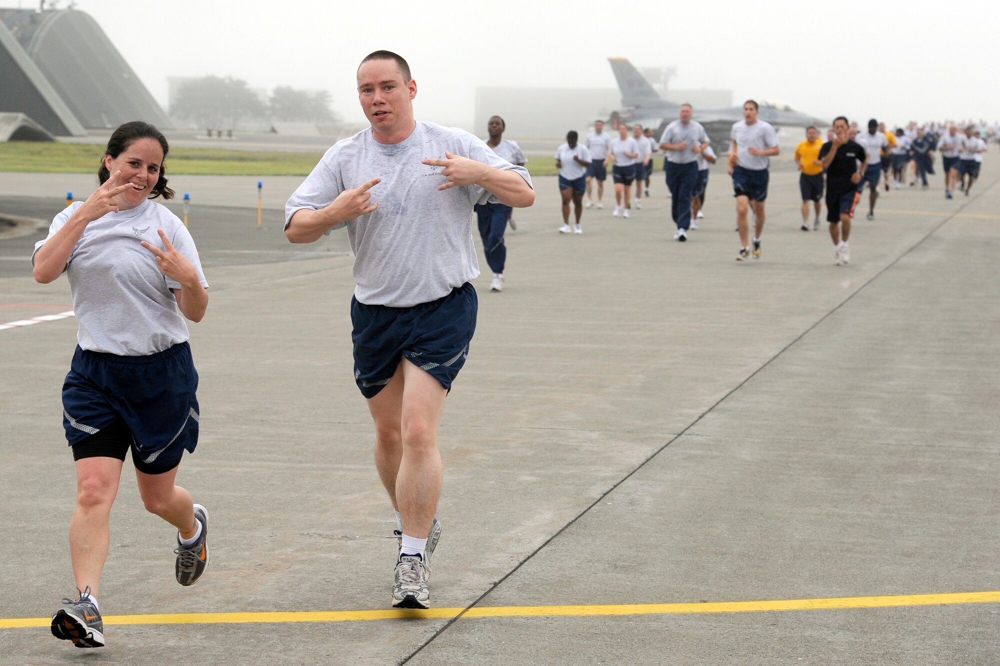 MISAWA AIR BASE, Japan -- Teresa Valdez, left, and Alexander Zybert, both from the 35th Operations Support Squadron, flash hand signs during the monthly readiness run Aug 5th. The readiness run is a monthly tradition on the base and is held to promote fitness and raise espirit de corps. (U.S. Air Force photo/Staff Sgt. Marie Brown/Released)