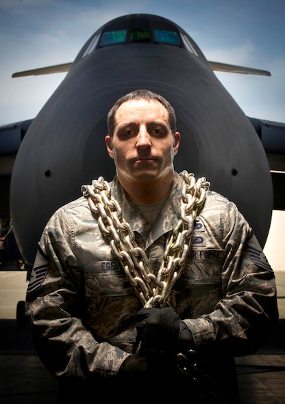 Master Sgt. Mark Eger and a C-5 Galaxy at Travis Air Force Base, CA on April 21, 2009. Sergeant Eger is with the 55th Aerial Port Squadron (AFRC) and was photographed to illustrate the natural strength and determined of the Travis aerial porters. They often work in the shadow of others or the dark of night, and literally shoulder the load and grip a single vision: Unrivaled Global Reach for America ... Always!   The photo's elements are meant to support their vision. The solitary person represents the strength of all aerial porters - without peers in this world - they are unrivaled. The C-5 Galaxy is one of the largest military aircraft in the world, unlimited in its range - Global Reach. All elements were made in America. The green light associated with night vision goggles represent their 24/7 operations and always ready for more. The chain, one of the prime tools of the trade, symbolizes all the events and actions of aerial porters who are linked by mission and each dedicated to getting resources where they need to be by working together. Their bond is their strength, spirit and purpose, as strong as the MB-2 chain and its 25,000 pound capacity. They are humble, sometimes taken for granted, yet ever present and ready to serve. Staff Sgt. Paul Sweeney, an instructor and designer for the Aerial port Operations Course, said in a 2008 Air Force print news article, "They (the duties of an aerial porter) include passenger service, fleet service, ramp, (the air terminal operations center), load planning, data records, cape forecasting, aerial delivery and cargo processing. We are responsible for getting all the air cargo and passengers to the fight and then getting them all home." The gigantic C-5 Galaxy, with its tremendous payload capability, provides the Air Mobility Command airlift in support of United States national defense. The C-5 can carry fully equipped combat-ready military units to any point in the world on short notice and then provide field support require