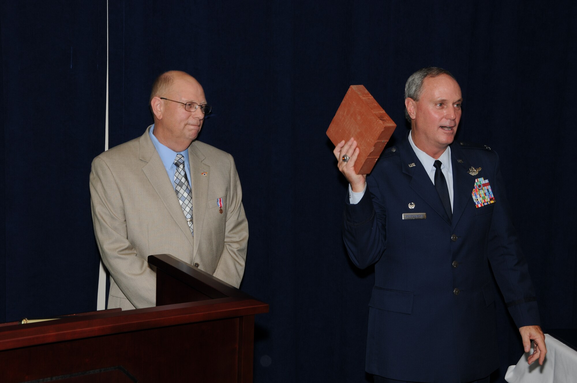 Colonel Harry D. Montgomery, 164th Airlift Wing Commander, presents a commemorative retiree brick that will encircle the historic fountain on base to Lieutenant Colonel Lamar Spencer during Col Spencer's retirement ceremony.