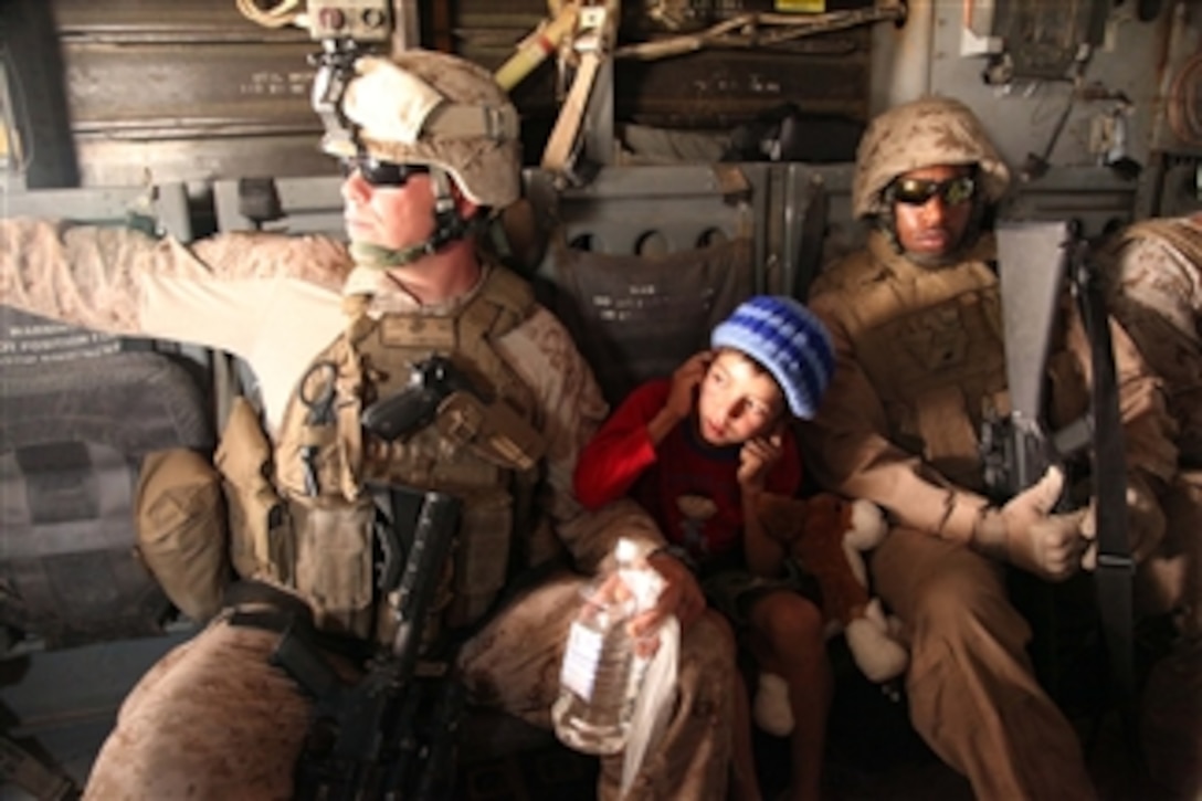 U.S. Marine Corps Staff Sgt. Jeff Liddic (left) and Lance Cpl. Thelonious Riddick escort Hayatullah, a 7-year-old Afghan boy, back to his village on a V-22 Osprey on Aug. 2, 2011.  Hayatullah was injured and flown to the Camp Bastion medical center where he received treatment for his injuries.  