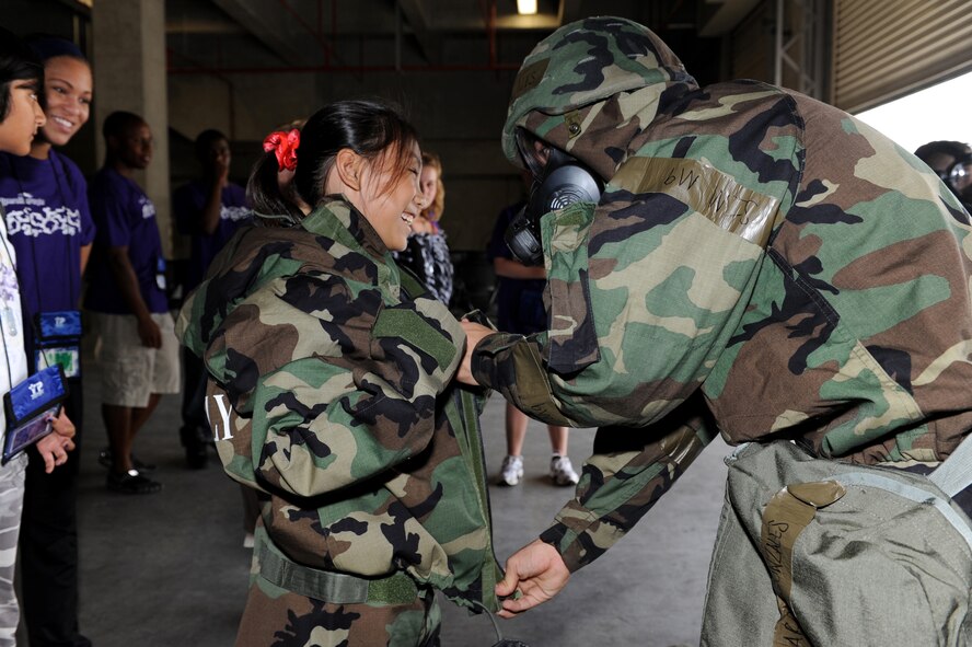 Lauren Param, Operation Purple Camp participant, tries on chemical gear with a helping hand from Airman 1st Class Aaron Gonzales, 18th Logistical Readiness Squadron technician, Aug. 1 at Kadena Air Base, Japan, during Operation Purple Camp. Children of U.S. military service members and Department of Defense personnel participated in demonstrations and briefings to illustrate how the deployment process works. Workers from the 18th Force Support Squadron also worked with participants to make Operation Purple Camp a success. (U.S. Air Force photo/Junko Kinjo)