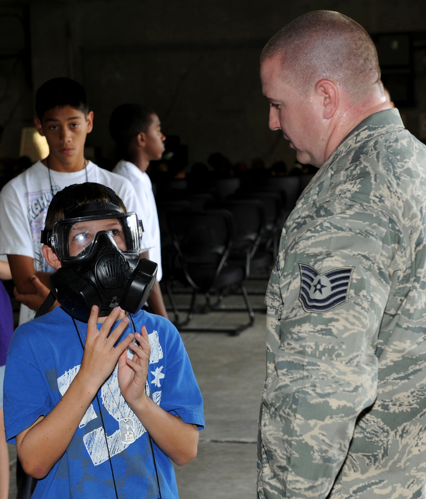 Tech. Sgt. Jeremy Ridgway, 18th Logistical Readiness Squadron technician, instructs Seth Werner, Operation Purple Camp participant, in how to put on a gas mask Aug. 1 at Kadena Air Base, Japan, during Operation Purple Camp. Children of U.S. military service members and Department of Defense personnel participated in demonstrations and briefings to illustrate how the deployment process works. Workers from the 18th Force Support Squadron also worked with participants to make Operation Purple Camp a success.  (U.S. Air Force photo/Junko Kinjo)