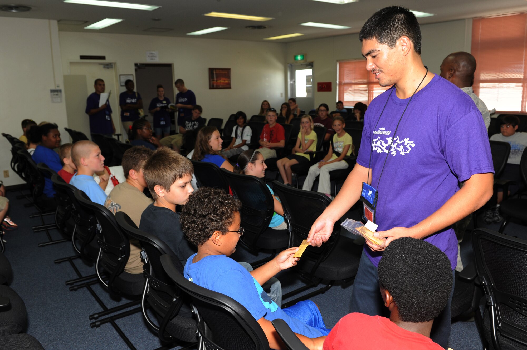 Justin Nguyen, a college student working at Shima No Ko Child Development Center, passes a dog tag to Marc Maschio, Operation Purple Camp participant, Aug. 1 at Kadena Air Base, Japan, during Operation Purple Camp. Children of U.S. military service members and Department of Defense personnel participated in demonstrations and briefings to illustrate how the deployment process works. Workers from the 18th Force Support Squadron also worked with participants to make Operation Purple Camp a success. (U.S. Air Force photo/Junko Kinjo)