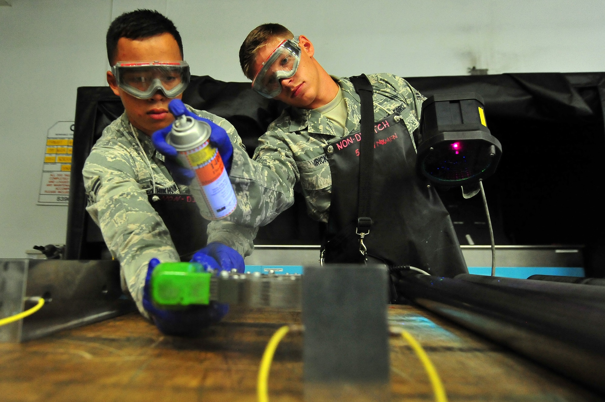 MINOT AIR FORCE BASE, N.D.  – Airman 1st Class Charles Sothikhoun, 5th Maintenance Squadron nondestructive inspection journeyman, and Airman 1st Class Jarred Irick 5th MXS NDI apprentice, spray down parts of a B-52H Stratofortress and perform a magnetic particle inspection allowing inspectors to track internal cracks and discontinuities within the equipment here, Aug. 8. NDI is the examination of aerospace weapon systems components and support equipment for structural integrity using nondestructive inspection methods and fluid analysis. (U.S. Air Force Photo/ Senior Airman Jesse Lopez)