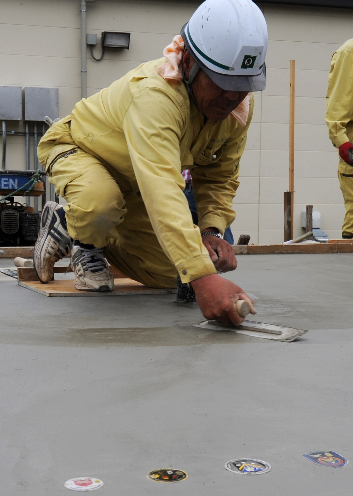 MISAWA AIR BASE, Japan -- A Japanese contractor smoothes the cement for a new antenna pad Aug. 2.  The coins laid in the cement represent Joint Tactical Ground Station operators from Delta Detachment, 1st Space Company, 1st Space Battalion, and 1st Space Brigade based out of Colorado Springs.  (U.S. Air Force photo/Staff Sgt. April Quintanilla)