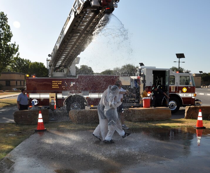 Air Force Reserve Tech. Sgt. Nitura Bender and Navy Master at Arms 1st Class Zachariah Janssen play the role of "victims" as they process through the first stage of decontamination under a fire hose during an emergency-response exercise Aug. 10, 2011, at Naval Air Station Fort Worth Joint Reserve Base, Texas.  Bender is a member of the 301st Civil Engineer Squadron while Janssen works in the Navy's security forces unit that guards the base.  Bender was simulating a broken leg and needed to be helped through the decontamination process for the exercise.  (U.S. Air Force photo/Laura Dermarderosiansmith)