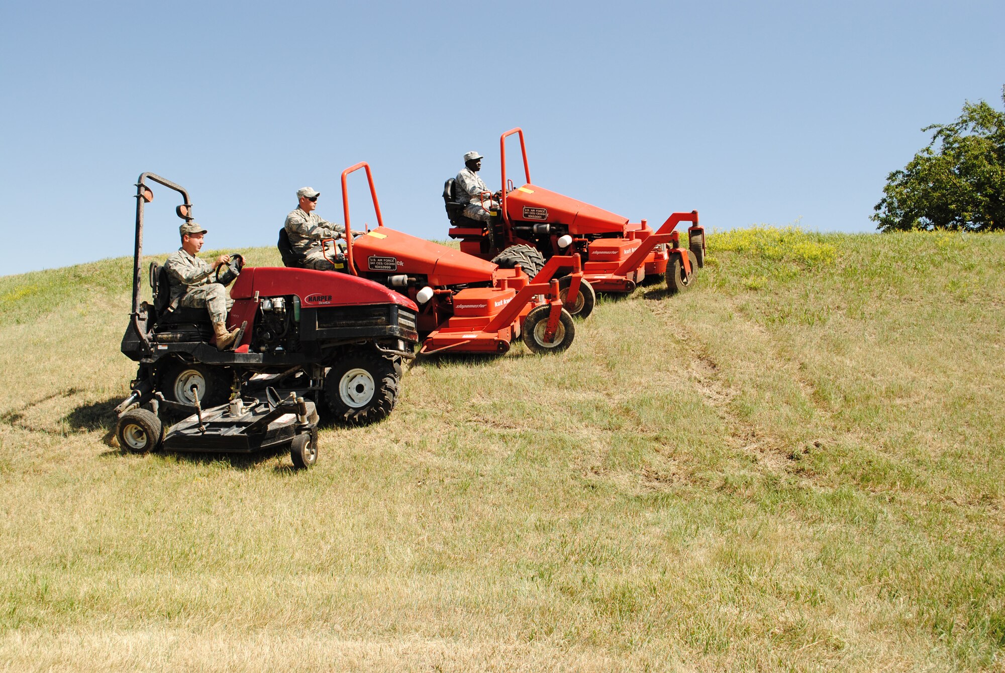 From left to right: Airmen 1st Class Logan Quibell, Cory Summers and Isaac Brenyah, 341st Civil Engineer Squadron pavement and construction equipment apprentices, mow a steep hill in formation.  Members of the 341st CES traveled to several launch facilities to clear overgrown vegetation to prevent alarms from going off.  (U.S. Air Force photo/Airman Cortney Paxton)