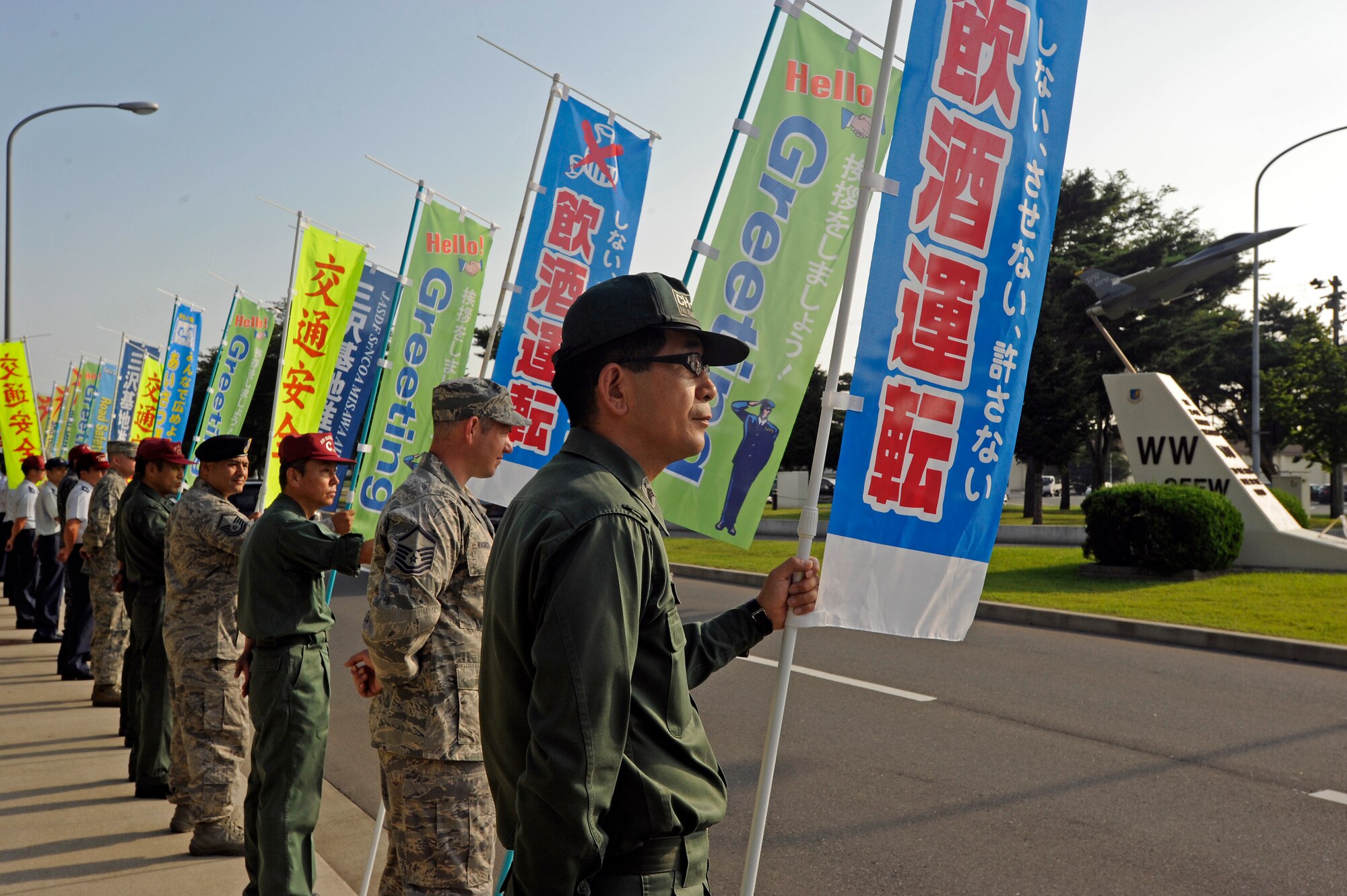 MISAWA AB, JAPAN -- MISAWA AB, JAPAN -- Japan Air Self-Defense Force, Chief Master Sergeant Kato (right) of the Senior Non-Commissioned Officer Association, United States Air Force, Master Sergeant Wagner (second from right) of the Misawa Top-Three Organization and Japan Air Self-Defense Force, Chief Master Sergeant Goto (third from right), participate in the monthly greeting campaign on 8 Aug.  The campaign encourages all pedestrian, bicycle and vehicle traffic entering the installation to not drink and drive and exchange a heartfelt "good morning." (U.S. Air Force photo by Master Sgt. Maria J. Bare/Released)